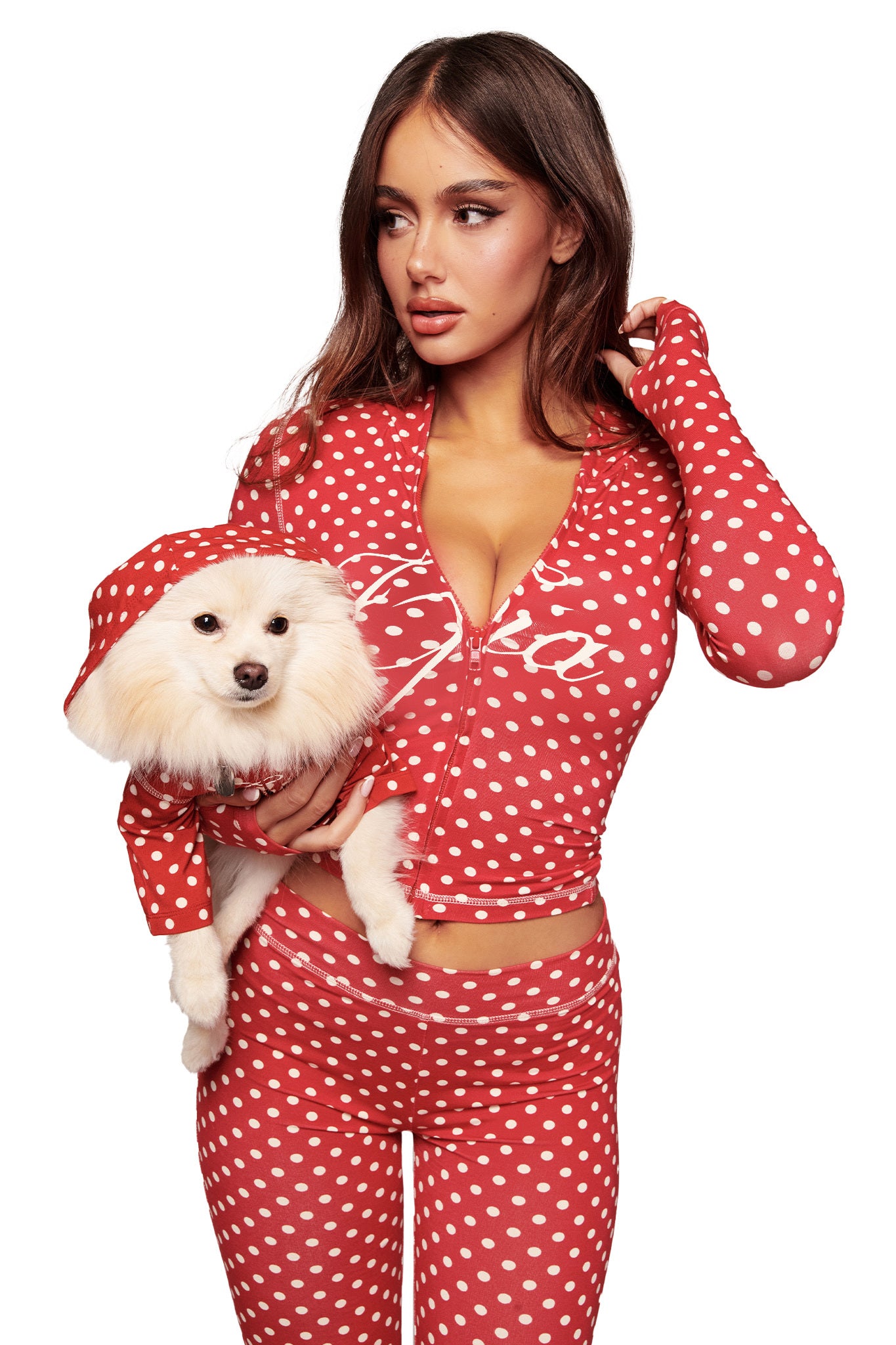 A woman in a red polka dot I.AM.GIA outfit with a zipper poses with her dog, who wears the I.AM.GIA BLARE BEST FRIEND DOG HOODIE - RED POLKA DOT. Both look off to the side against a white background.