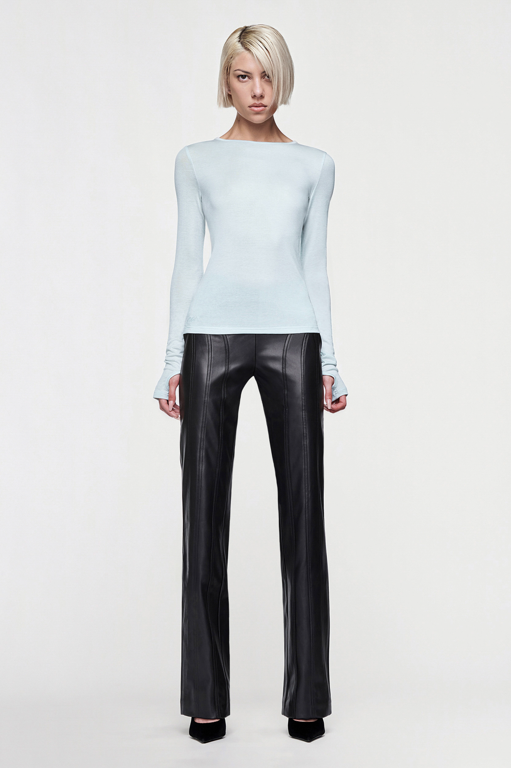 A person with short blond hair faces forward, wearing the CDP CLAUDIA LONG SLEEVE BASIC TOP in eggshell blue and black leather pants with vertical seams, set against a plain light background.