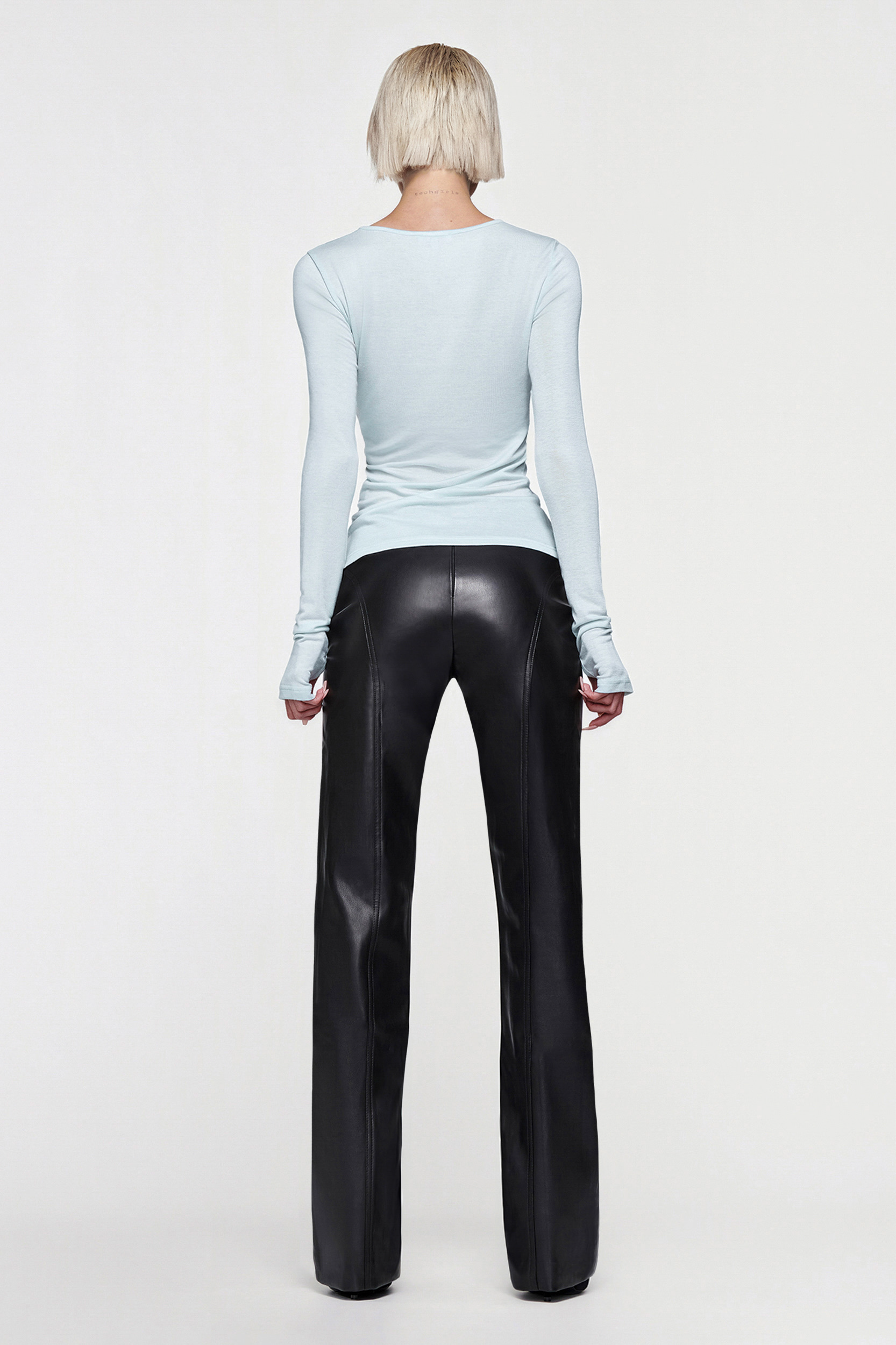 A person with short blonde hair, seen from behind, is wearing the CDP CLAUDIA LONG SLEEVE BASIC TOP in eggshell blue and black leather pants against a plain white background.