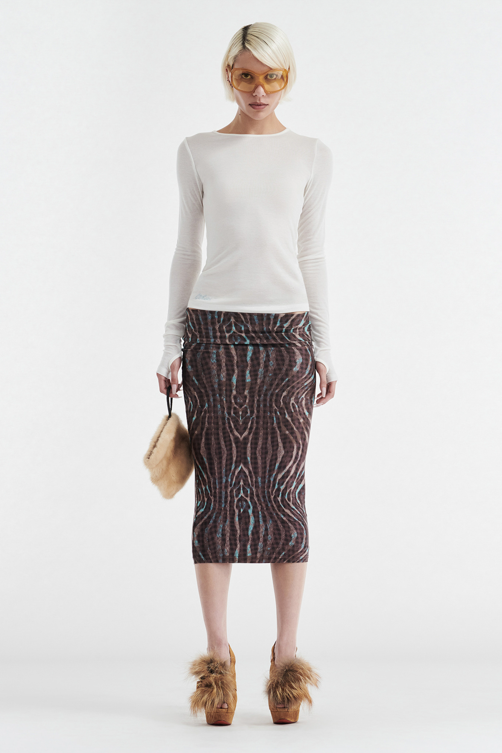 A person wears the CDP CLAUDIA LONG SLEEVE BASIC TOP - WHITE with orange sunglasses, a brown patterned midi skirt, brown furry platform shoes, and holds a small beige furry bag against a plain white background.