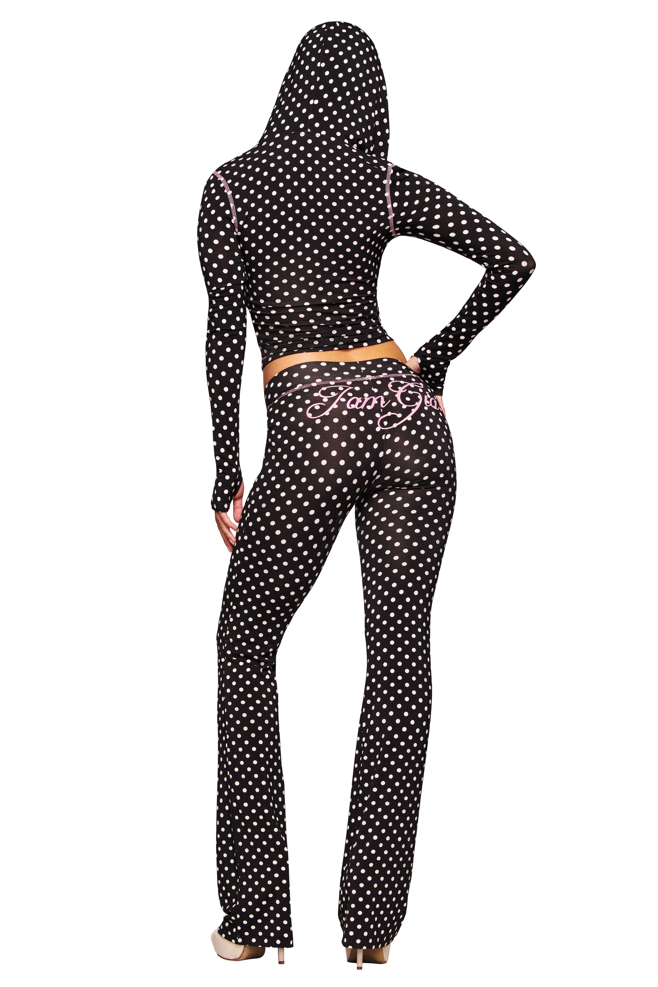 A person wears the I.AM.GIA BLARE HOODIE - BLACK POLKA DOT, featuring a bodycon fit and white polka dots. "Fairy Girl" in pink decorates the back of the pants. The hood is up, and they're wearing heels, facing away from the camera.