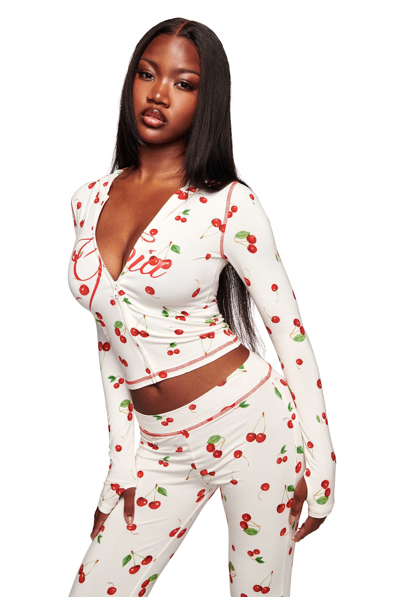 A woman models the I.AM.GIA BLARE HOODIE - CHERRY ON TOP, a white, long-sleeve fitted hoodie with cherry print, paired with matching pants. She stands against a plain white background with long straight hair.