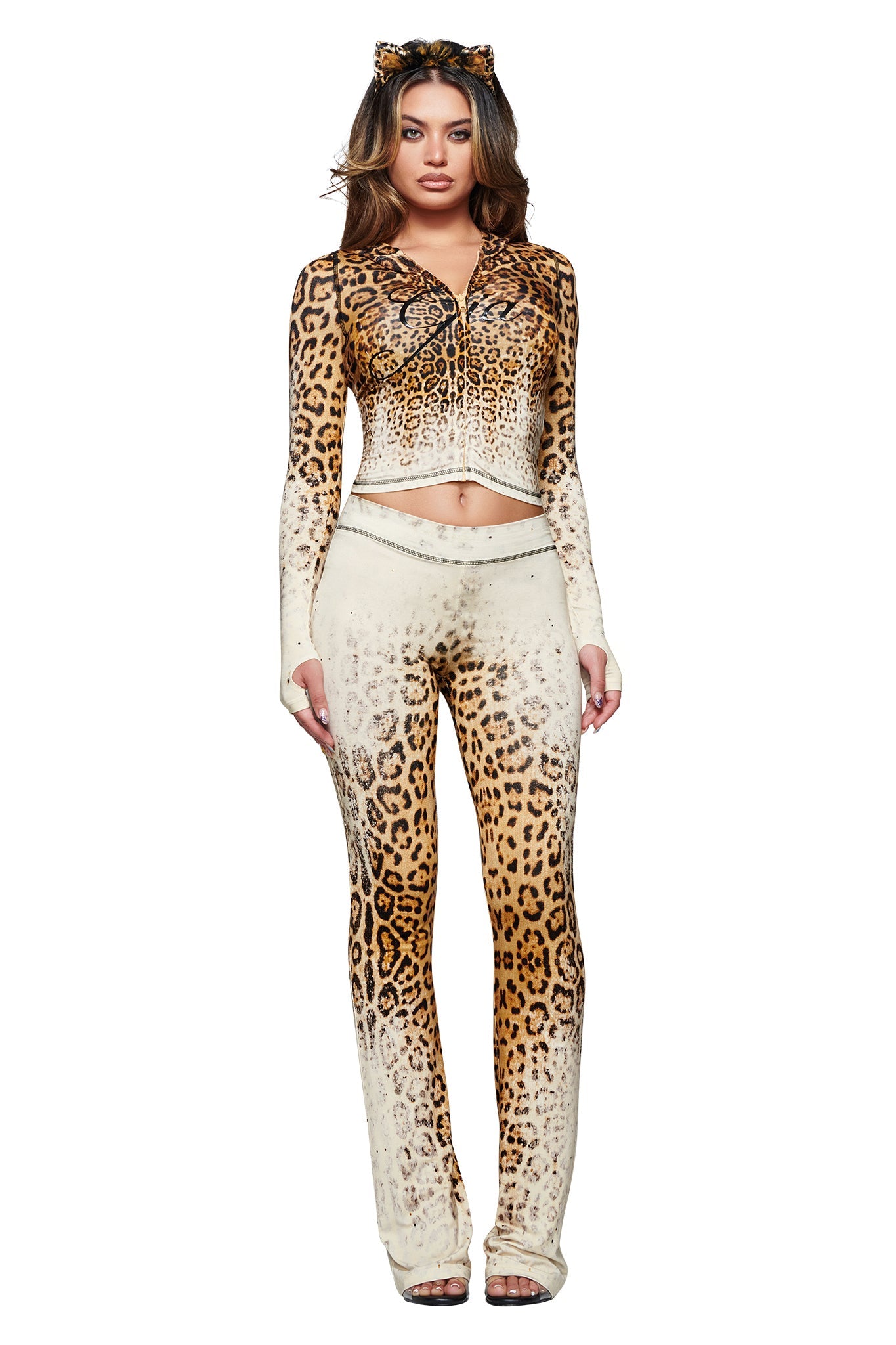 A woman stands against a white background wearing the I.AM.GIA BLARE HOODIE in Cream Faded Panthera, styled with matching leopard print pants and cat ears headband for a coordinated look.