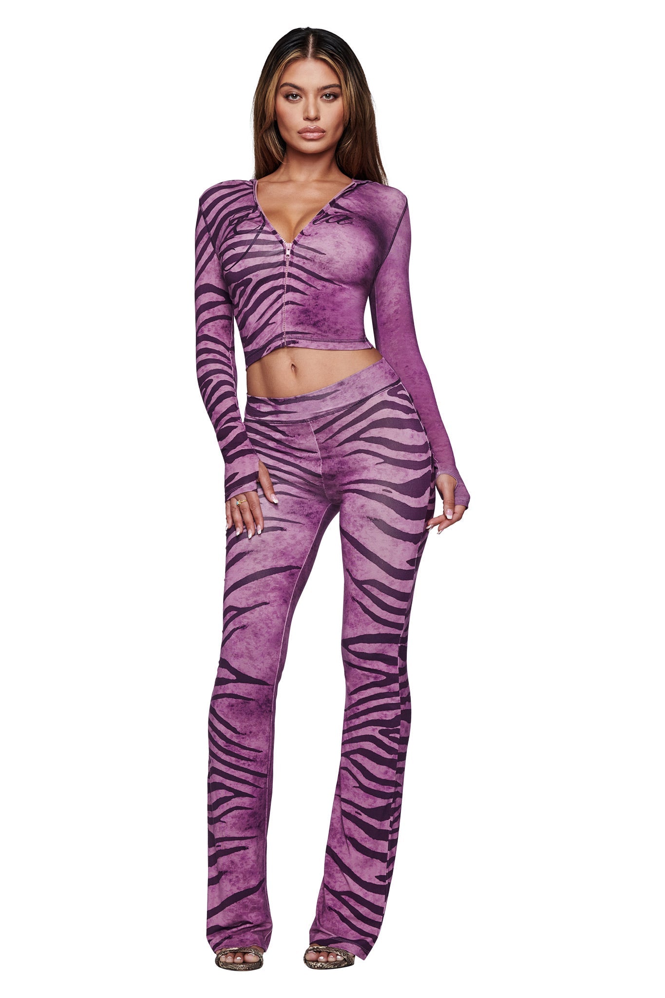 A woman faces forward wearing the I.AM.GIA BLARE HOODIE in Plum Wild Side zebra print, paired with matching flared pants. With long brown hair and open-toed shoes, she radiates bold energy in this standout set.