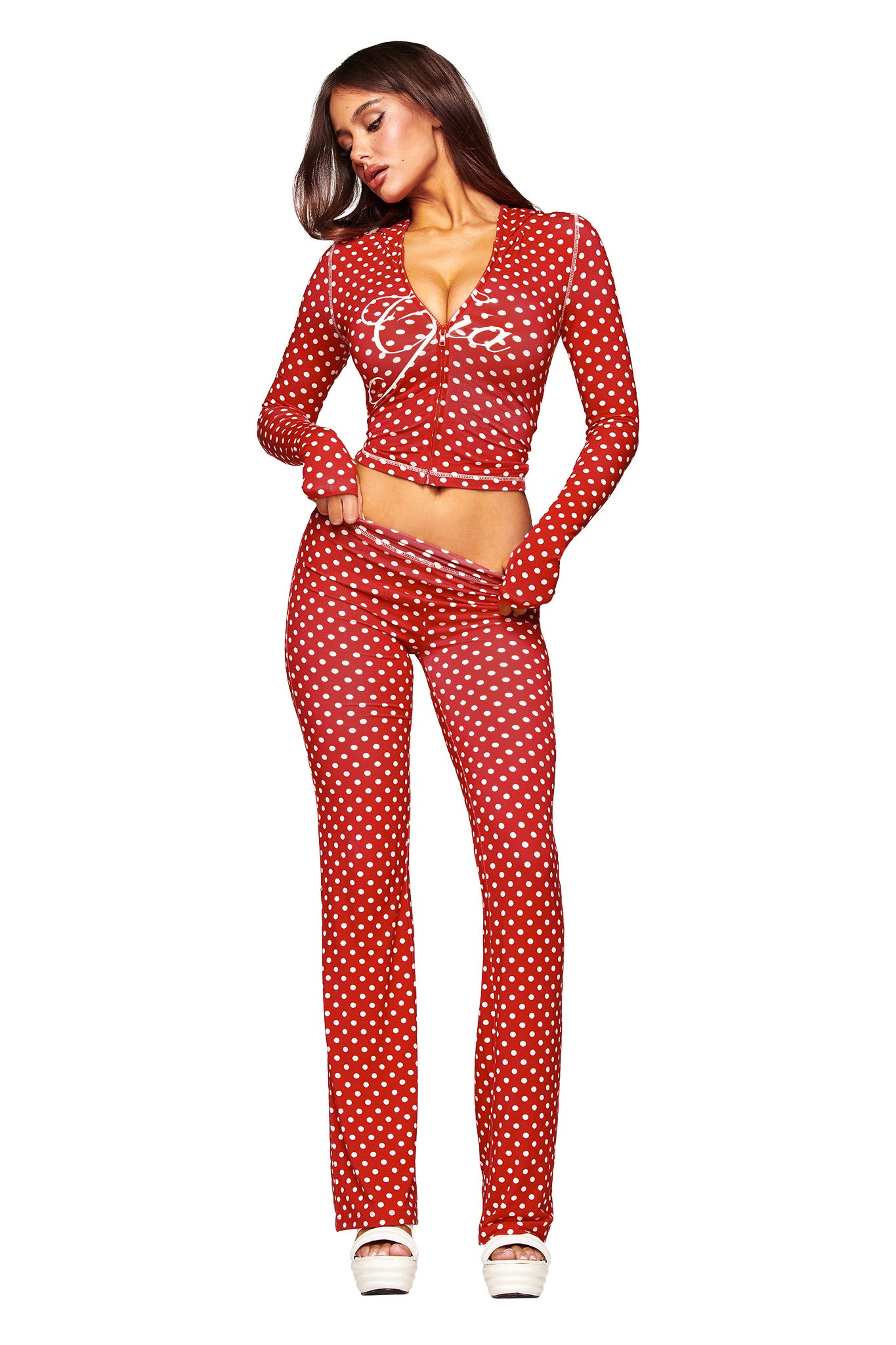 A woman poses in a red polka dot, long-sleeve crop top and matching I.AM.GIA BLARE TRACKPANT - RED POLKA DOT, paired with white platform shoes against a plain white background.