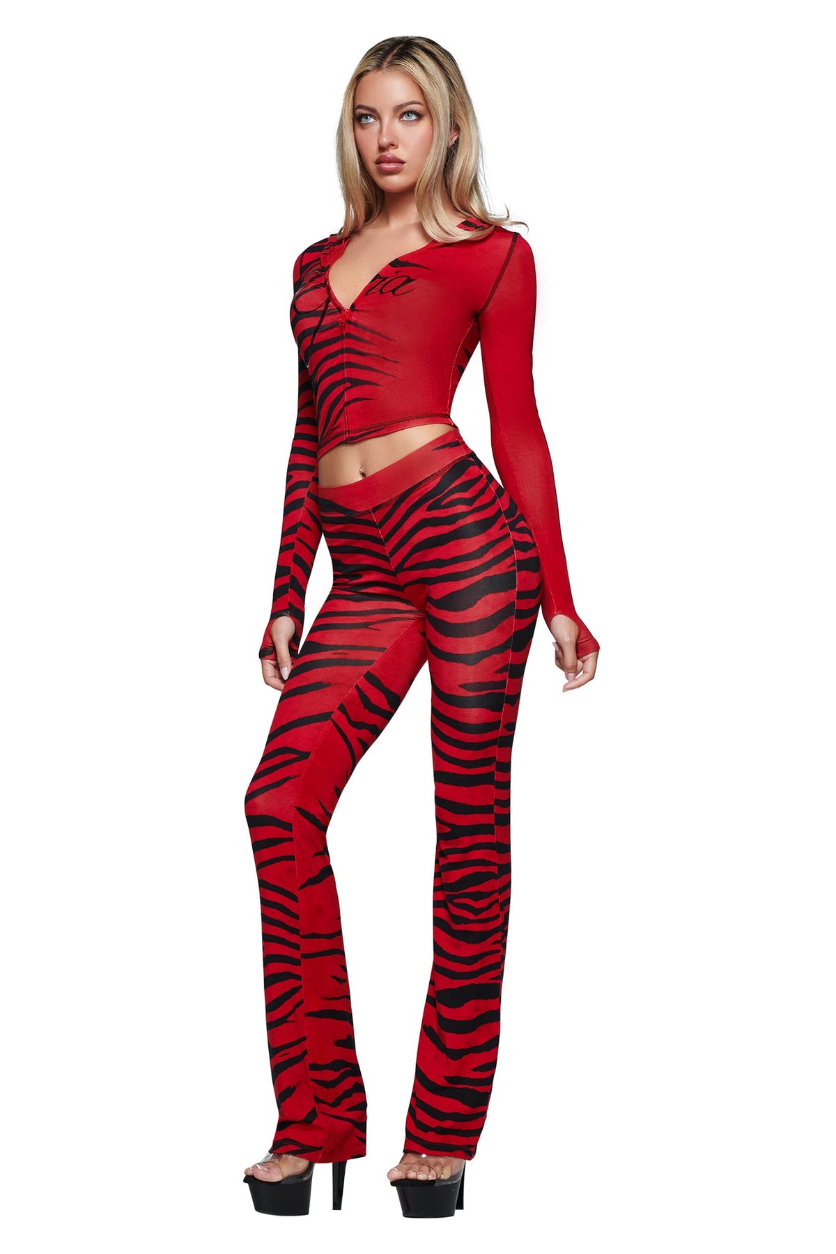 A woman is wearing the I.AM.GIA BLARE TRACKPANT - RED WILD SIDE, a striking red and black matching set with a long sleeve crop top and flared pants, styled with black high heels against a white background.