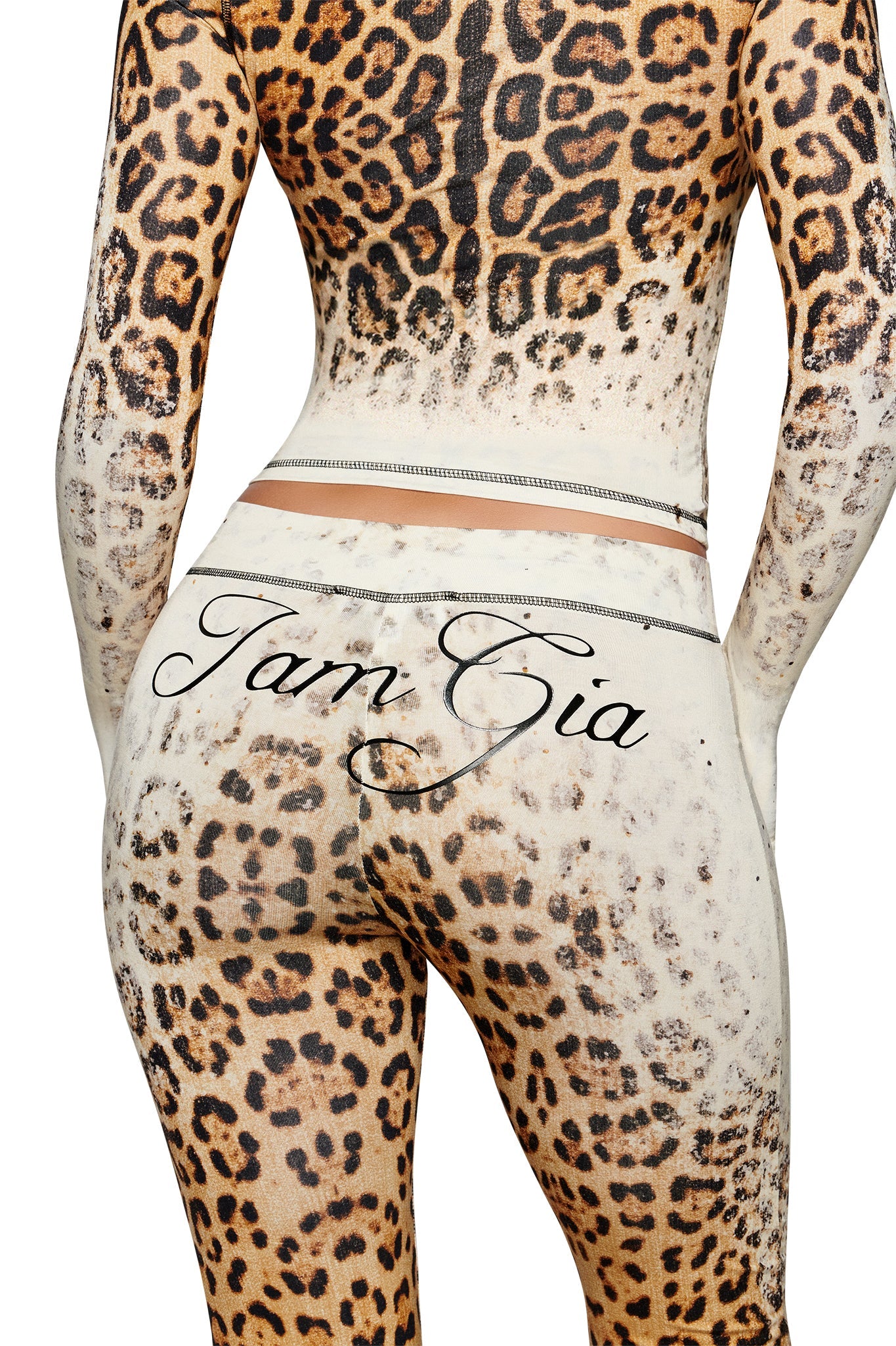 A person is wearing the I.AM.GIA BLARE TRACKPANT in Cream Faded Panthera, featuring a bold leopard-inspired print and the “Tam Gia” script on the back just above the hips. The look channels I.AM.GIA’s signature eye-catching style, with particular emphasis on striking details around the lower back and waist.