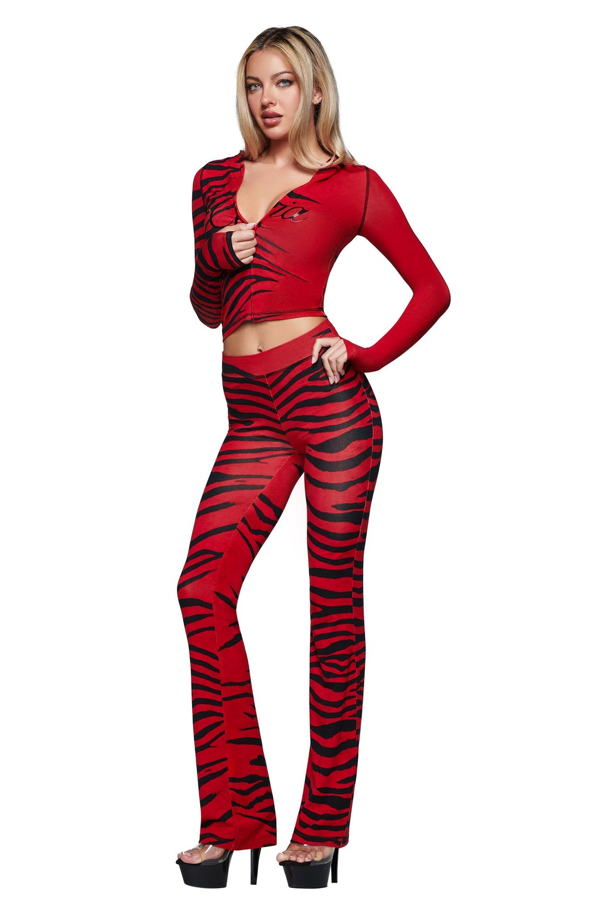 A woman stands in platform heels against a white background, wearing the I.AM.GIA BLARE TRACKPANT in Red Wild Side—a striking red and black zebra print sheer pant with flared legs and long sleeves.