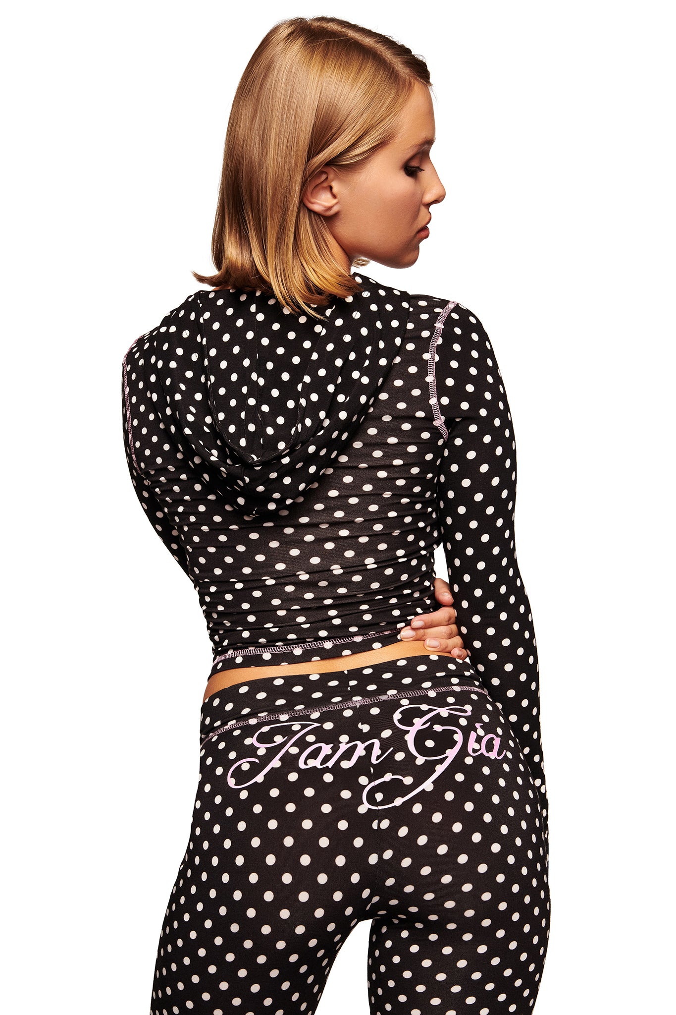 A person with short blonde hair wears the I.AM.GIA BLARE HOODIE in black polka dot and matching pants featuring "Fam Gia" in cursive on the back, against a white background.