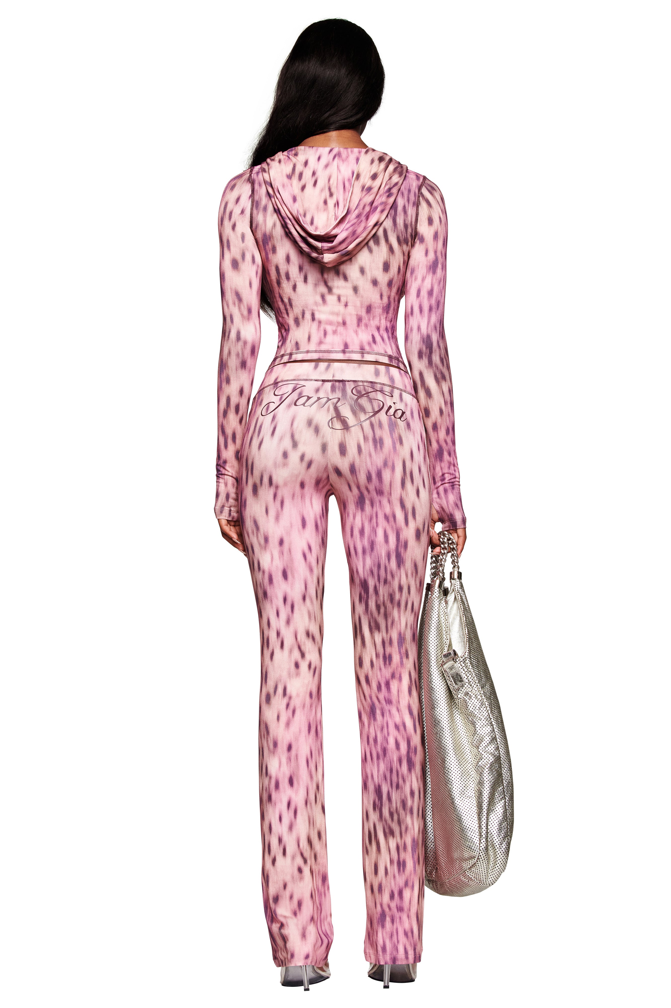 A woman faces away, wearing the I.AM.GIA BLARE HOODIE in Pink Blurred Cheetah. She holds a large silver textured bag in her left hand and pairs the look with heels.