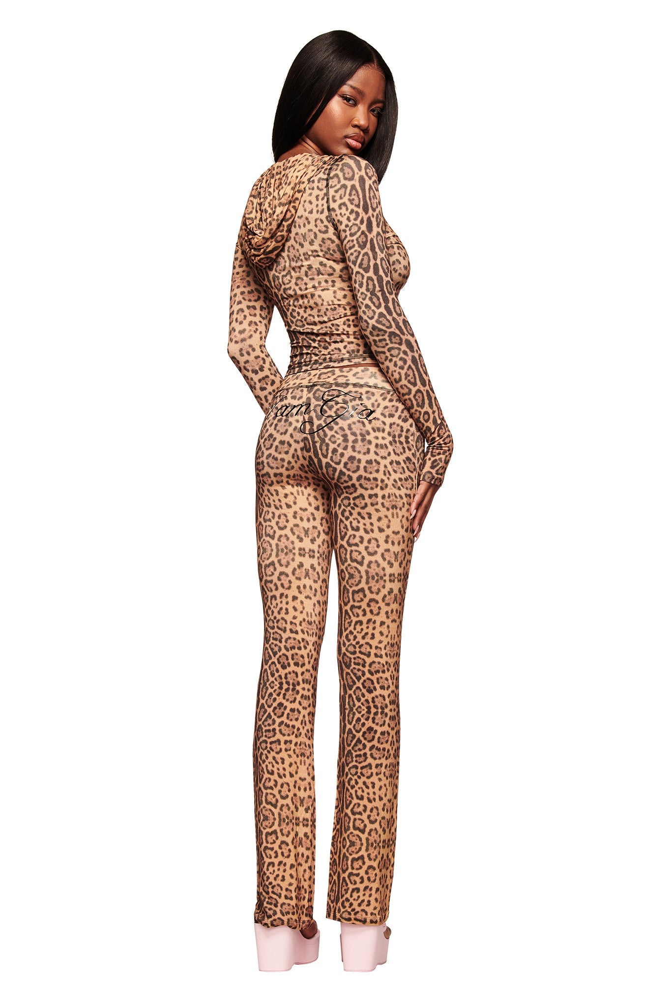 A woman poses in I.AM.GIA's BLARE TRACKPANT - PANTHERA, featuring a fitted cheetah-print design, as she looks over her shoulder against a seamless white background.