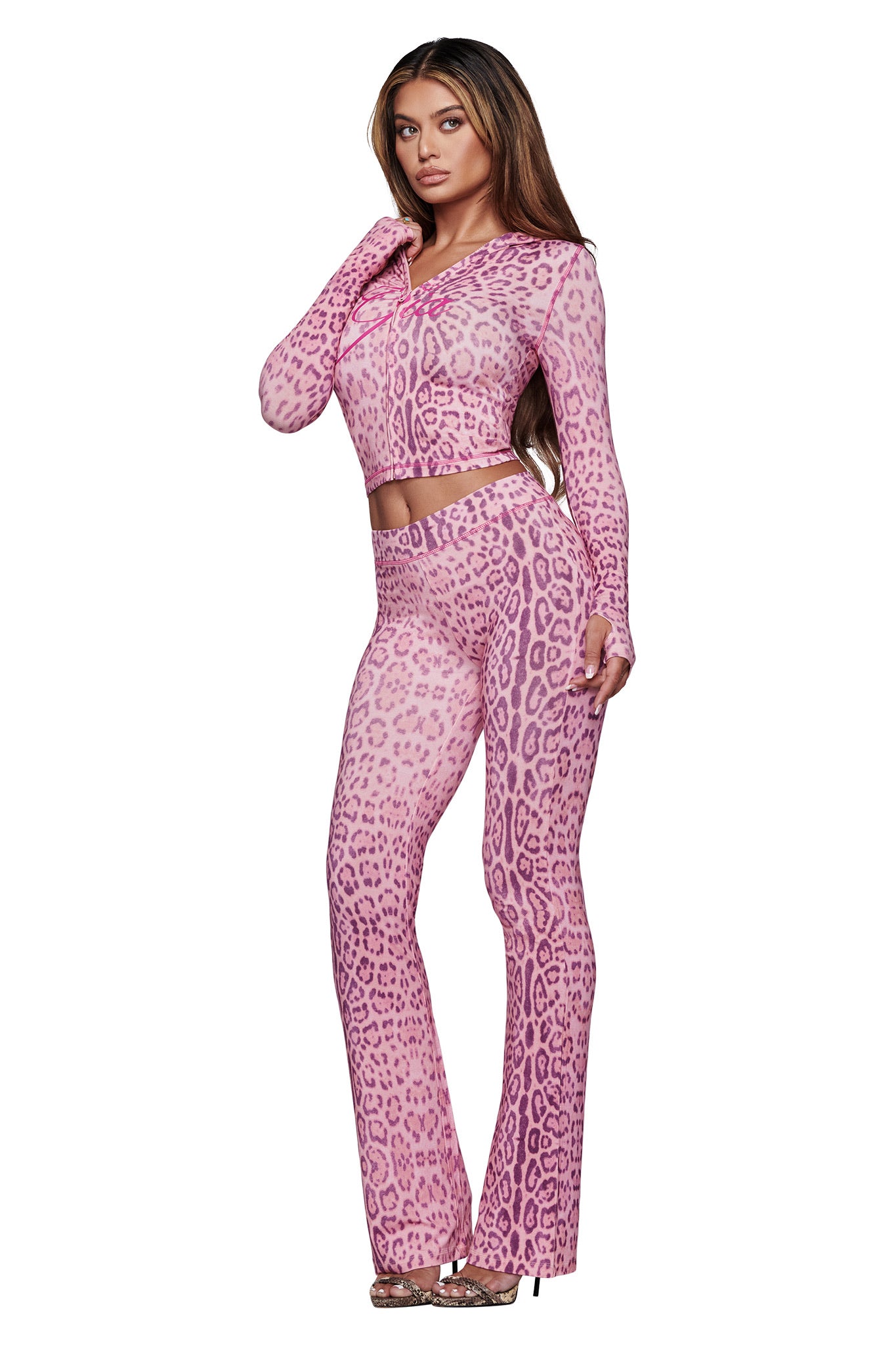 A woman poses against a white background wearing the I.AM.GIA BLARE TRACKPANT in Pink Panthera with a matching long-sleeve fitted crop top and heels.