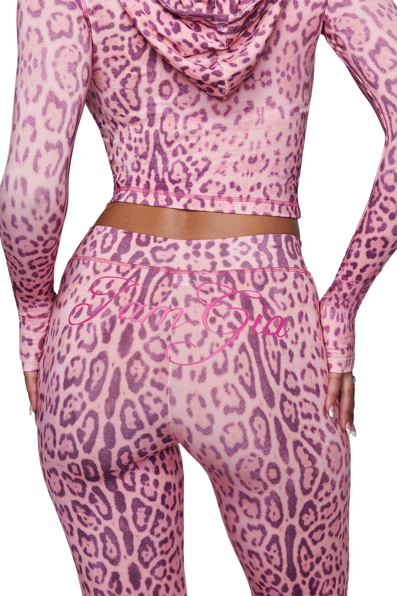 A person is shown from the back wearing I.AM.GIA’s BLARE TRACKPANT - PINK PANTHERA, featuring a matching hooded crop top and flared leggings with “Icon Gym” scripted on the waistband.