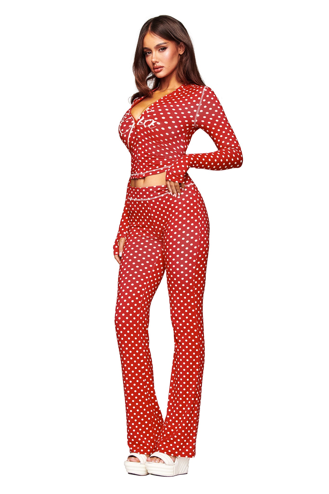 A woman poses in the I.AM.GIA BLARE HOODIE - RED POLKA DOT and matching flared pants with white spots, paired with white platform shoes, against a plain white background.