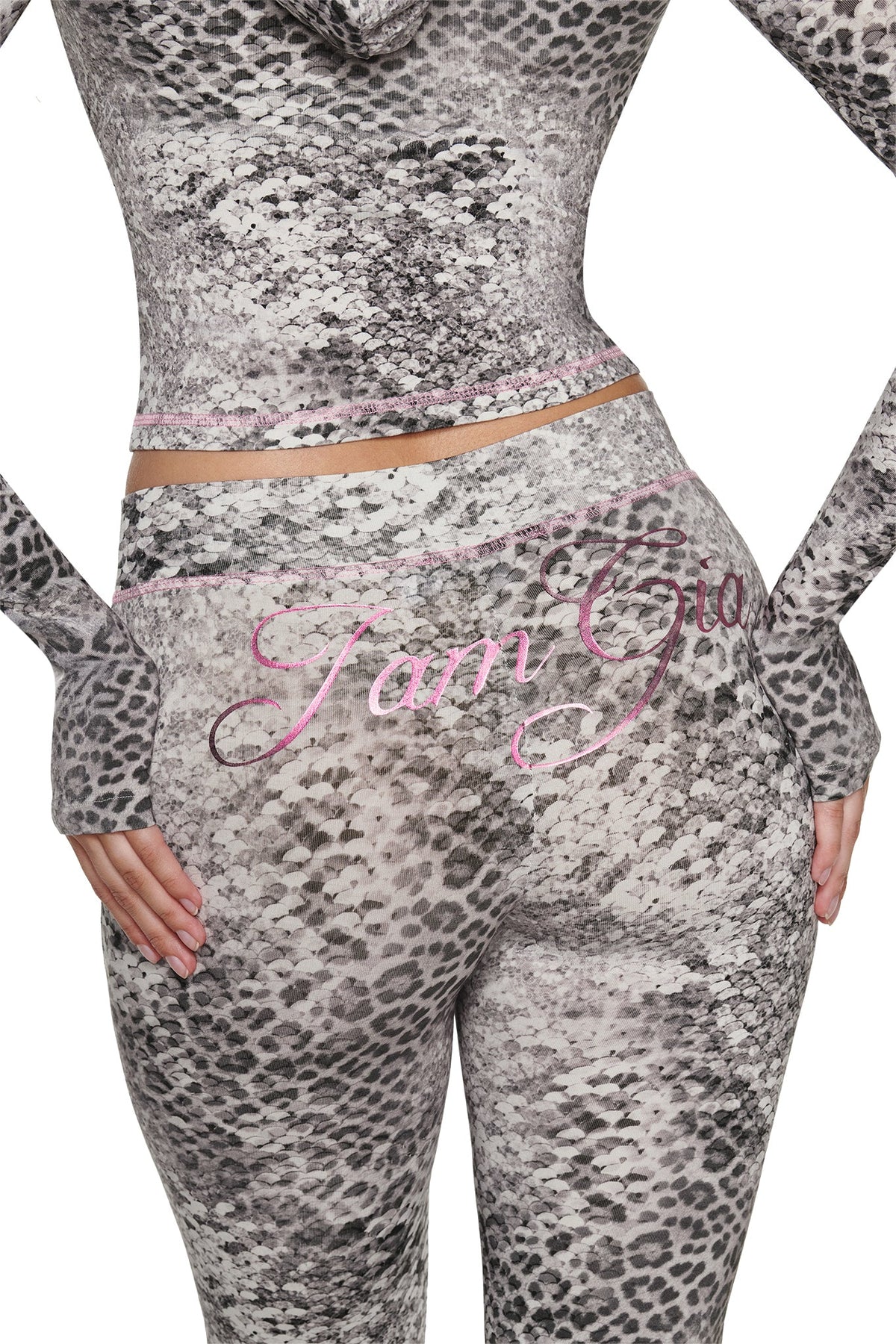High-waisted BLARE TRACKPANT - SILVER LUXE LEOPARD and a matching long-sleeve top in a grey and black leopard print, featuring pink stitching and “I am Gia” embroidered in pink script across the back.