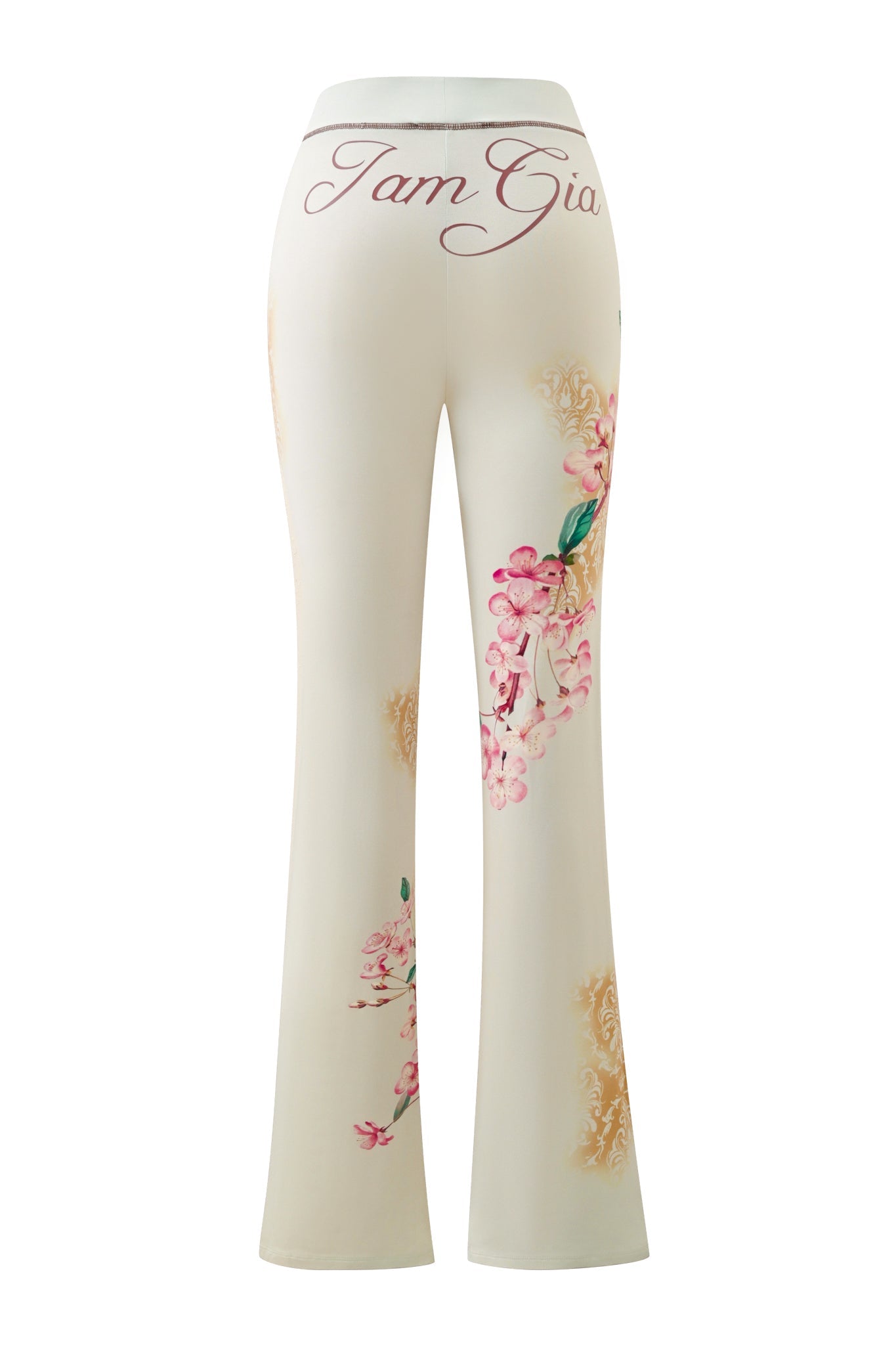 The BLARE TRACKPANT - BLOSSOM by I.AM.GIA are white, high-waisted trackpants featuring a pink floral print with gold accents and “Tam Gia” written in cursive across the back waistband.