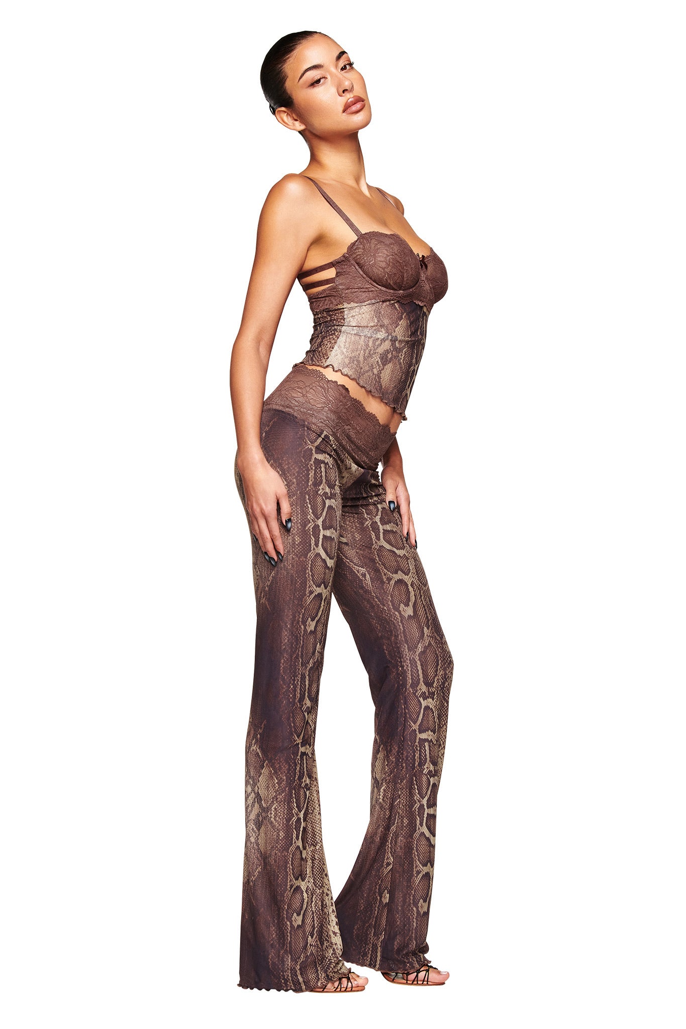 A woman models the I.AM.GIA SILO TOP - SNAKE, a brown snake print, fitted camisole-style mesh bustier top, paired with flared pants. She stands sideways with one hand on her hip against a white background.