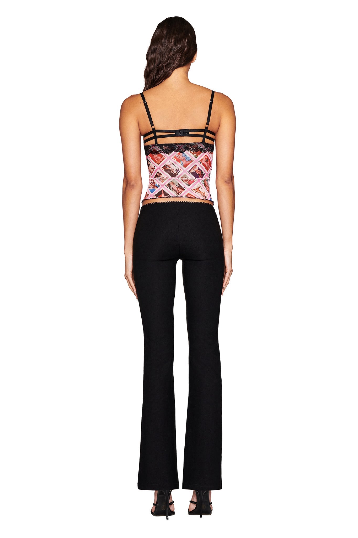 With their long dark hair facing away, the individual stands against a white background in black flared pants and an I.AM.GIA SILO TOP in a multi-color geometric Gia Face Card print.