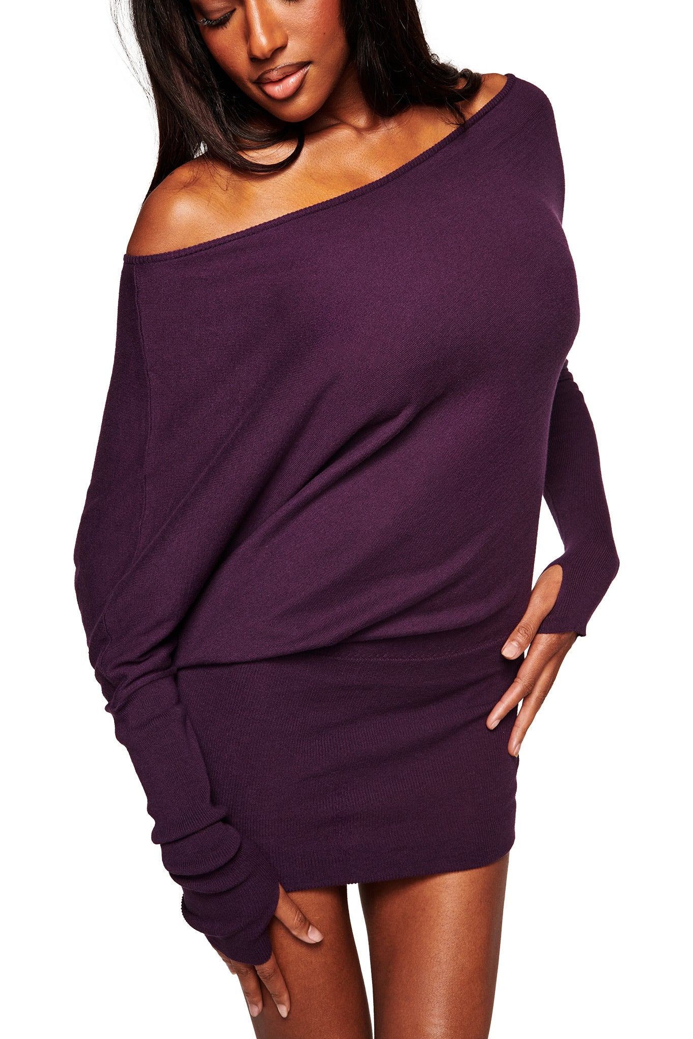 A woman stands against a white background wearing the I.AM.GIA GISELLE MINI DRESS in plum, an off-the-shoulder sweater dress with long sleeves, one sleeve pulled over her hand.