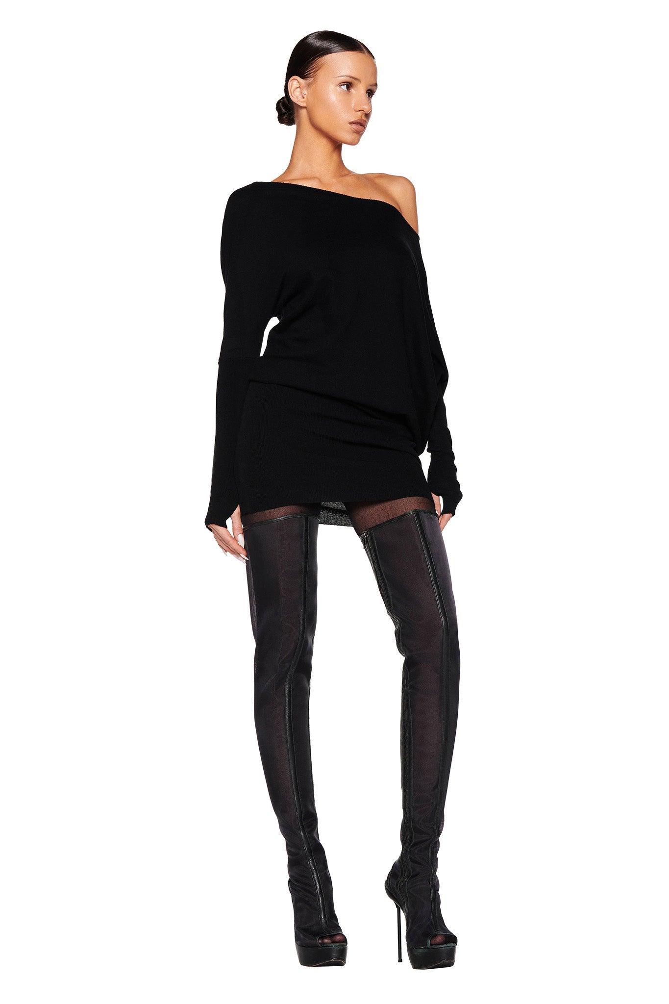 A woman with slicked-back hair stands confidently, wearing an I.AM.GIA GISELLE MINI DRESS in black and thigh-high black boots with platform heels. She is looking to the left, with arms relaxed by her sides on a white background.