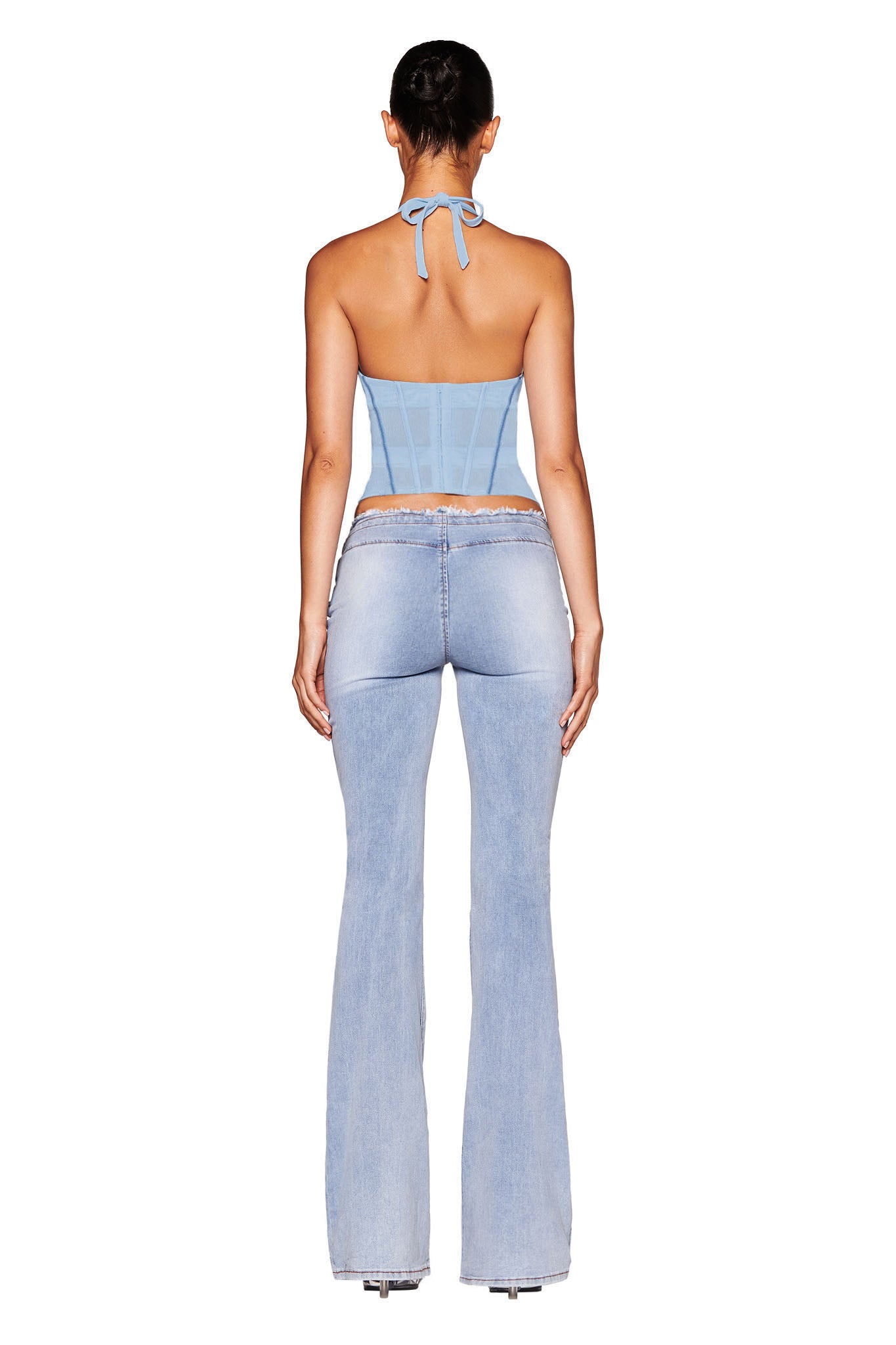 Rear view of a person wearing the LOLA Corset Top in Baby Blue by I.AM.GIA, featuring satin bust cups paired with light blue flared jeans. Their hair is styled in a sleek bun against a plain white background, emphasizing the outfit.