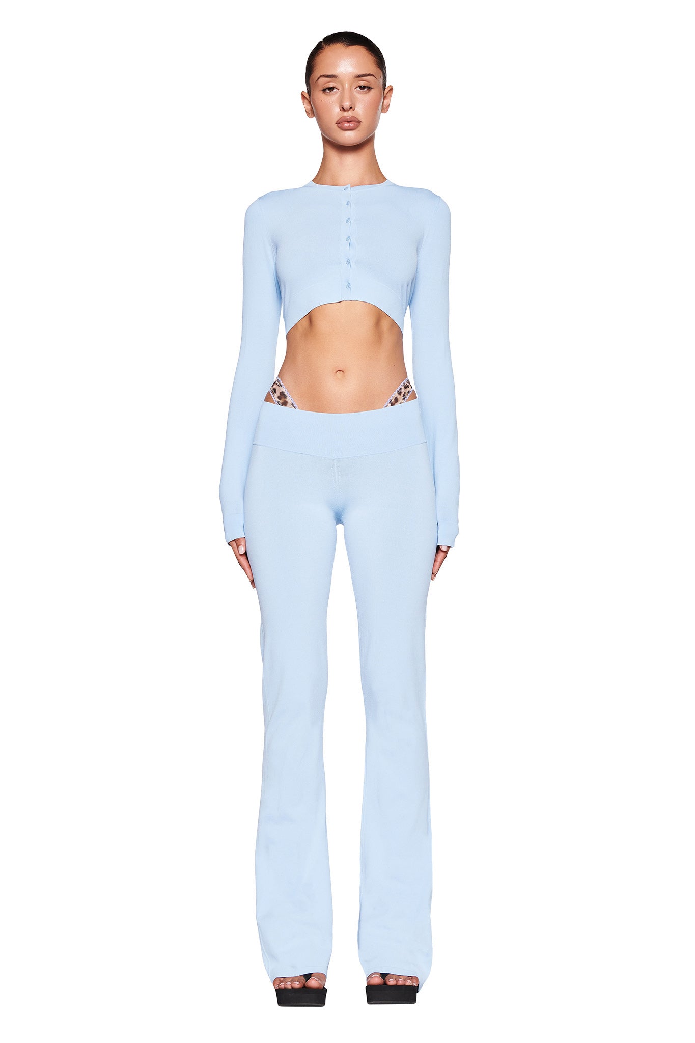 A woman stands against a plain white background wearing a light blue, long-sleeve, cropped button-up top and matching I.AM.GIA AUDRINA PANT in Powder Blue. She has black high-heeled shoes and is posing with her arms relaxed by her sides.