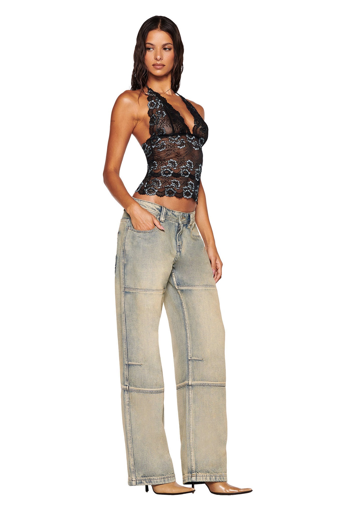 A woman with wet-look hair wears a black lace halter top and I.AM.GIA MISTY JEAN - TAN 2.0 light-wash, low-rise, wide-leg jeans with visible seams. She stands in profile, one hand in her pocket, against a white background.