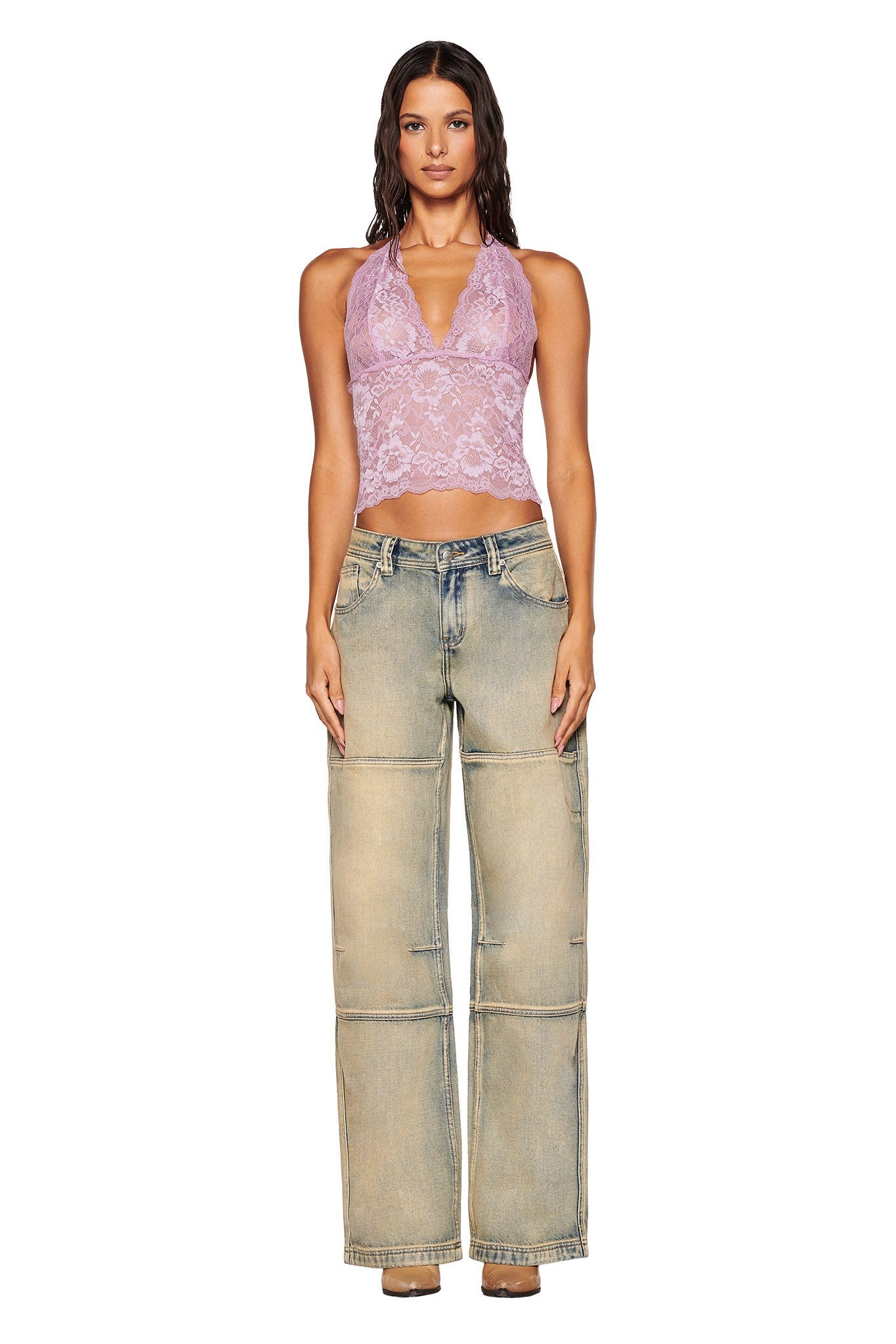 A woman is wearing the GEM HALTER TOP - PURPLE : LILAC by I.AM.GIA, featuring sheer lace detailing, paired with wide-legged, faded denim jeans. She stands against a plain white background, looking directly at the camera.