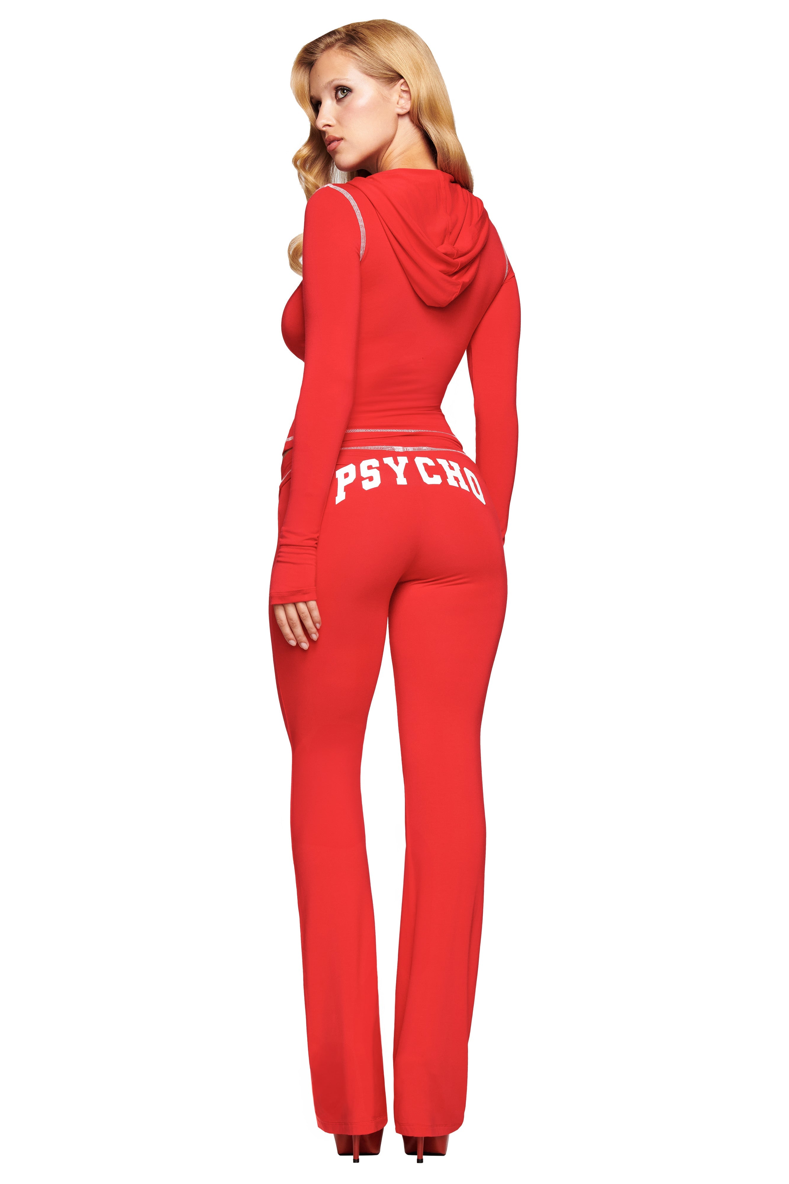 A woman with long blonde hair wears fitted red I.AM.GIA BLARE TRACKPANT - PSYCHO : SALSA, featuring "PSYCHO" in white across the back as she faces away from the camera.