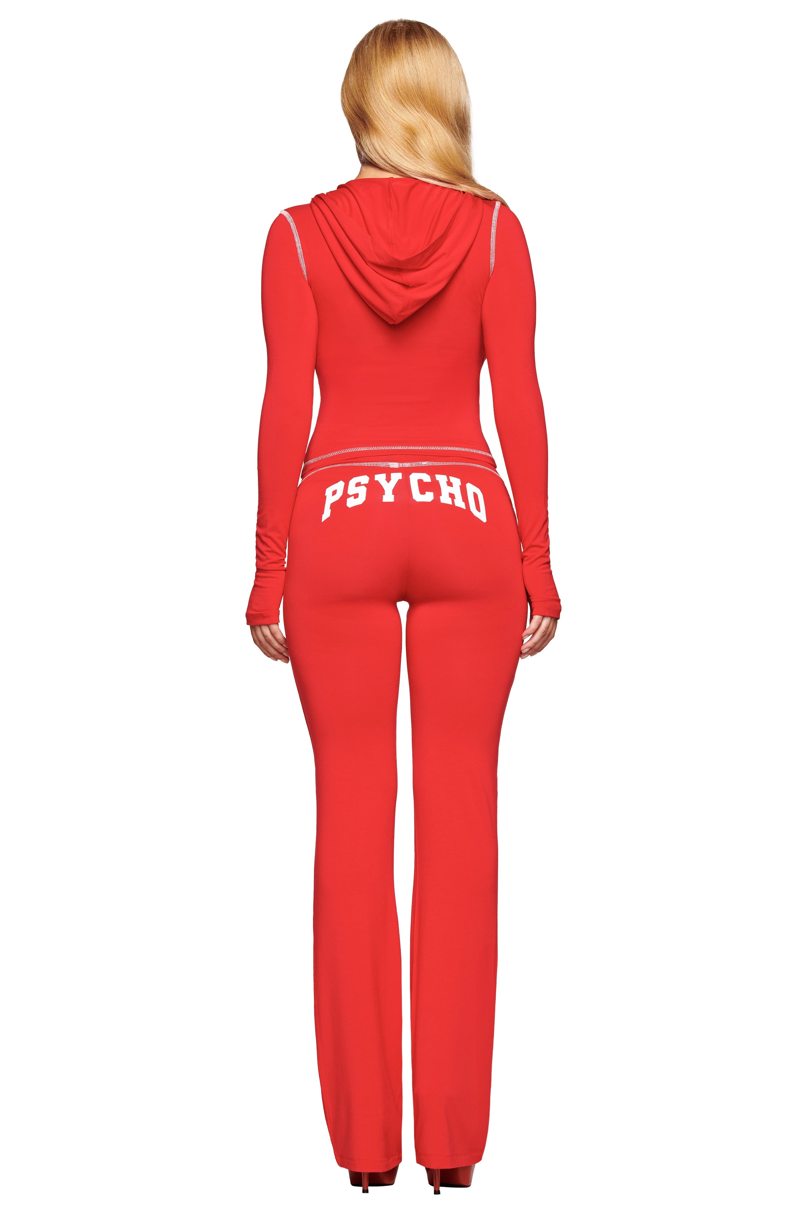 A woman with long blonde hair models fitted red I.AM.GIA BLARE TRACKPANTS—featuring “PSYCHO” in white across the back—as she stands facing away from the camera.