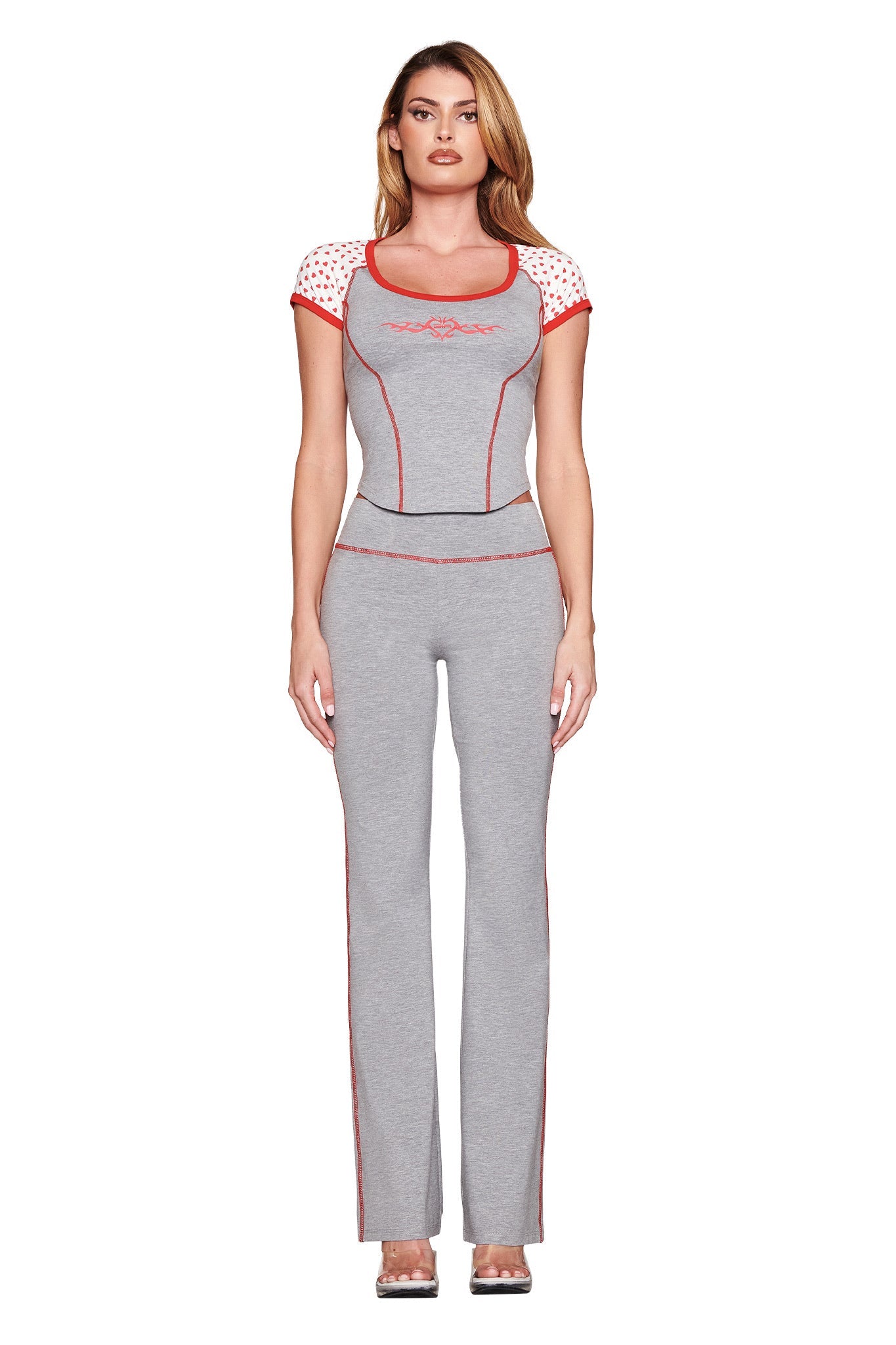 A confident woman poses in an I.AM.GIA ASHTIN TOP in heather grey, featuring a bodycon fit with red trim and playful white polka dots on a red raglan ringer tee style. Her long hair is styled neatly against a white background.