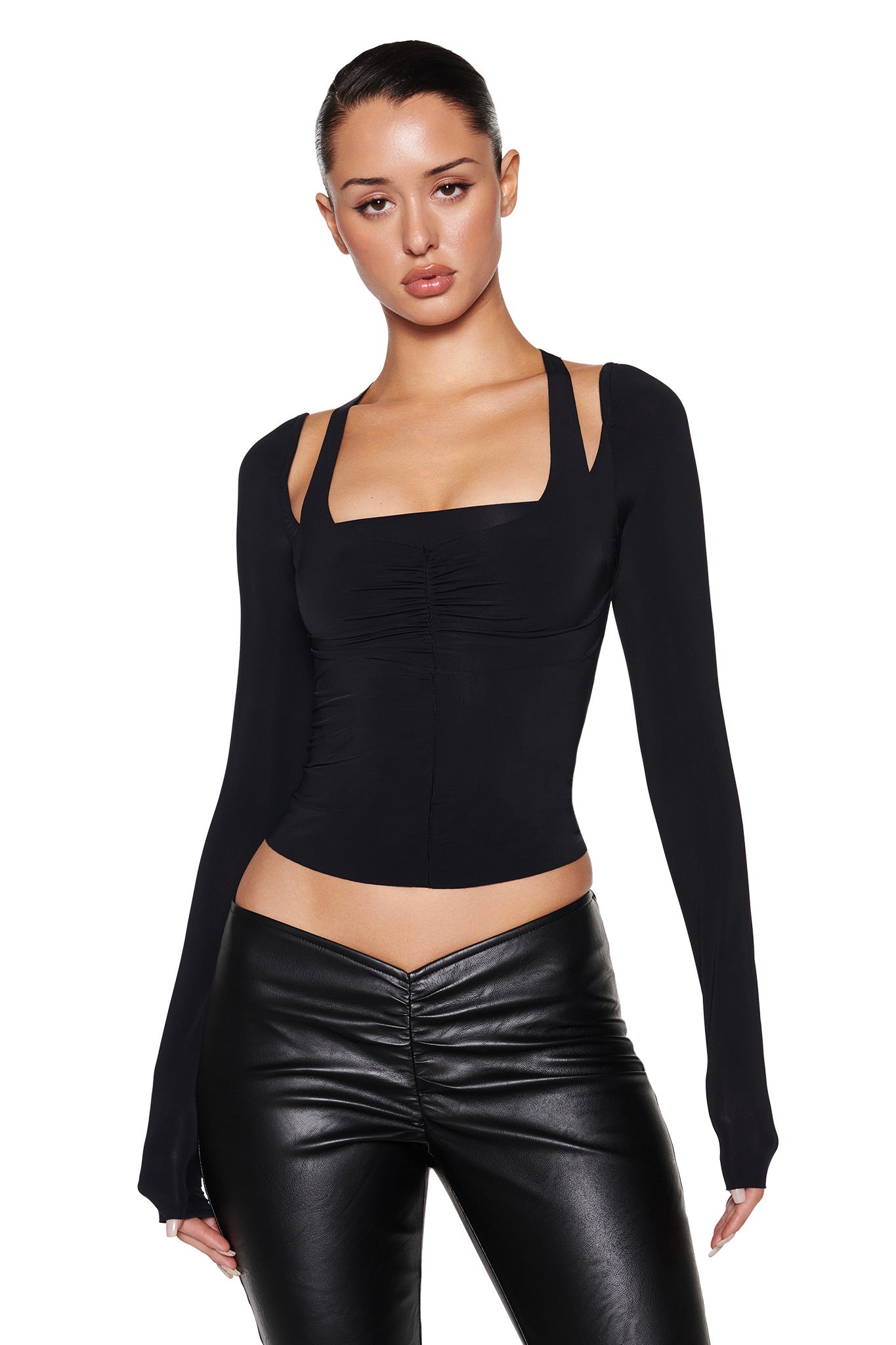 Against a plain white background, a person with slicked-back hair wears I.AM.GIA's fitted black NERINA LONG SLEEVE TOP featuring a square neckline and high-stretch black leather pants.