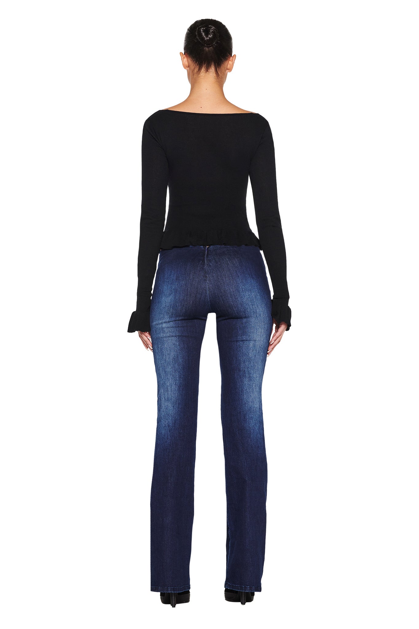 Rear view of a person in I.AM.GIA's RAVEN TOP - BLACK and blue flared jeans, black shoes, against a plain white background with hair styled in an updo.