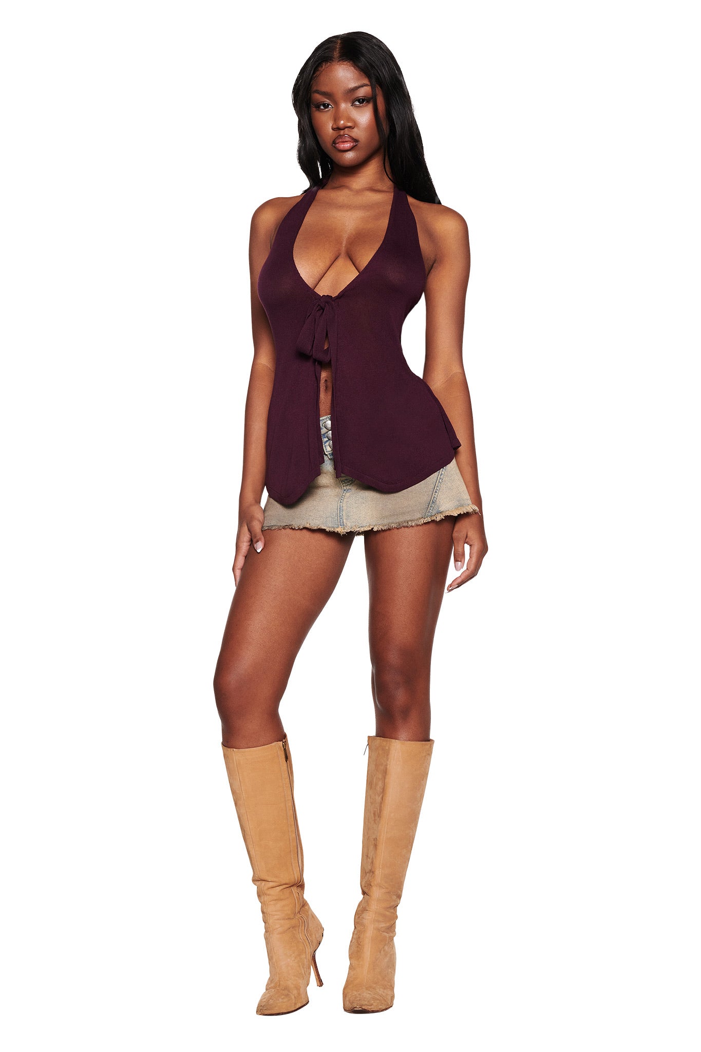 A person models the I.AM.GIA SIMI TOP - PURPLE: PLUM, a sleeveless tie-front halter top, paired with denim shorts and tan knee-high boots. They stand against a white background, highlighting the plunging V neckline of this chic outfit.
