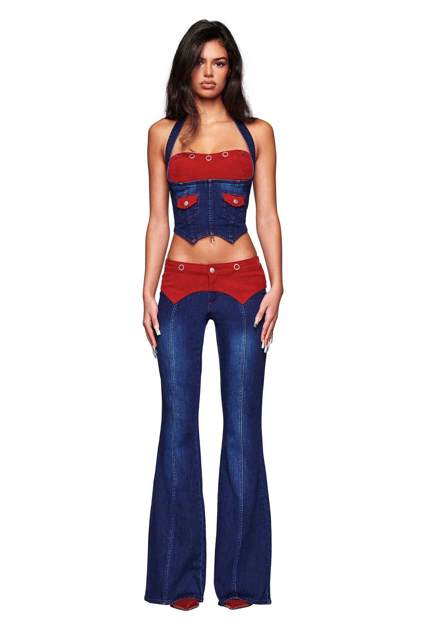 A woman faces forward in the I.AM.GIA TOMMIE CORSET - DARK WASH RUBY, a unique dark wash denim halter corset crop top with button details and red accents, paired with matching high-waisted flared jeans against a plain white background.