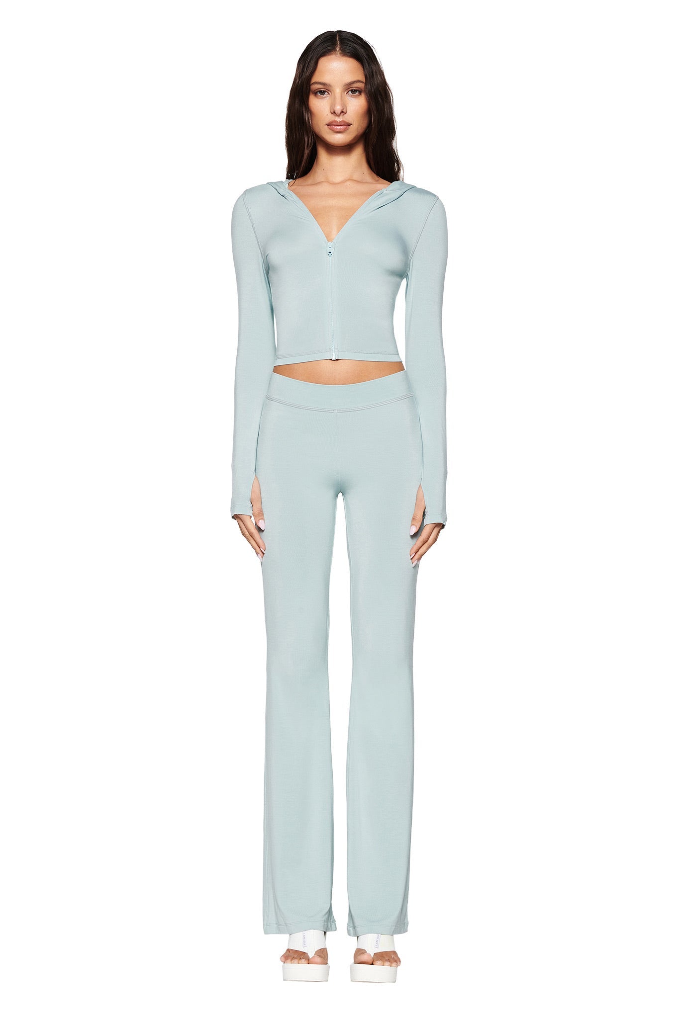 A woman dressed in I.AM.GIA’s seafoam BLARE HOODIE and matching high-waisted trousers stands facing forward against a white background, pairing the look with open-toe heels and radiating elegance and style.