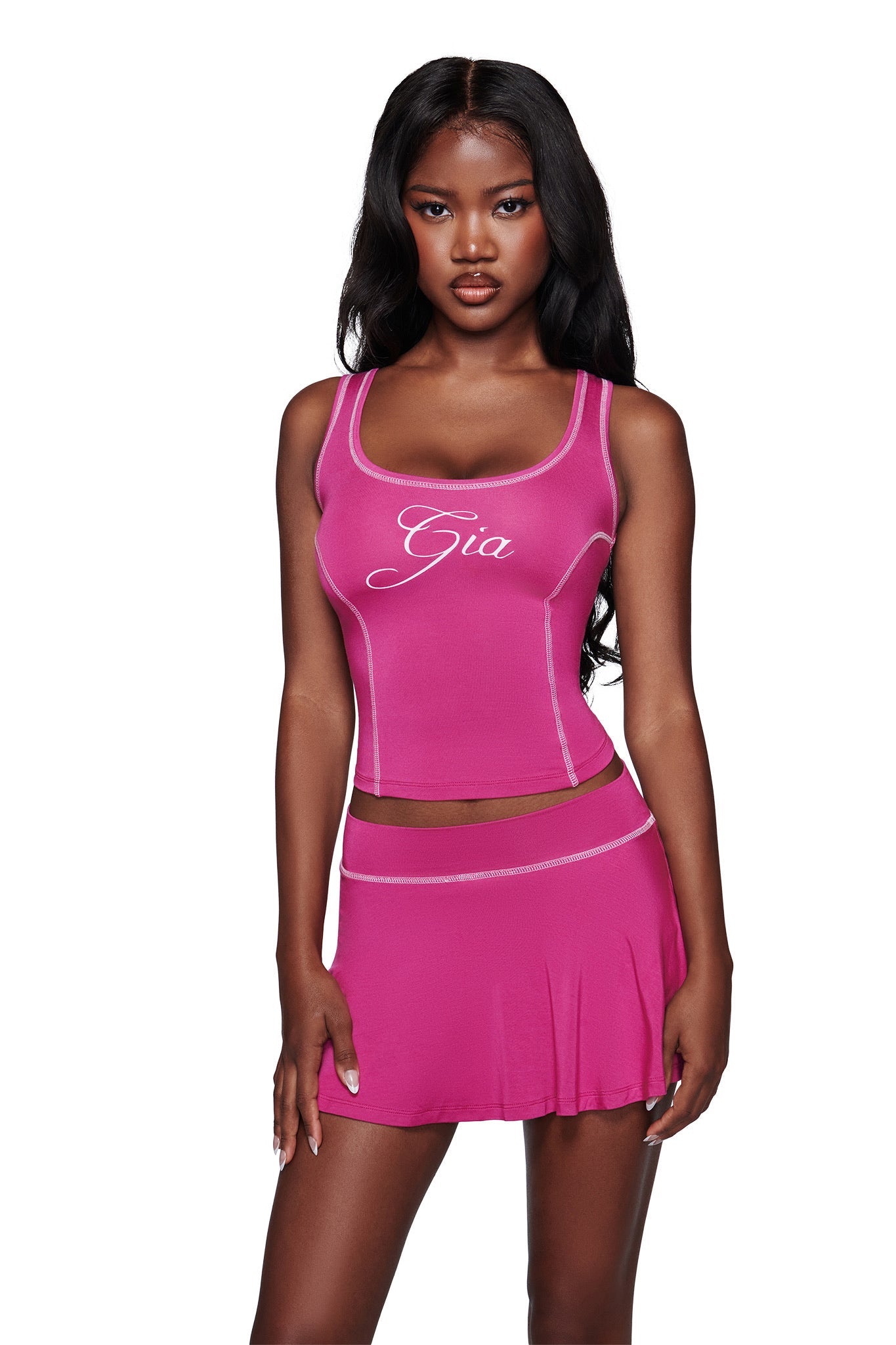 A woman in a bright pink I.AM.GIA tank top with "Gia" in cursive and the I.AM.GIA BLARE SKORT - RASPBERRY, posing against a white background.
