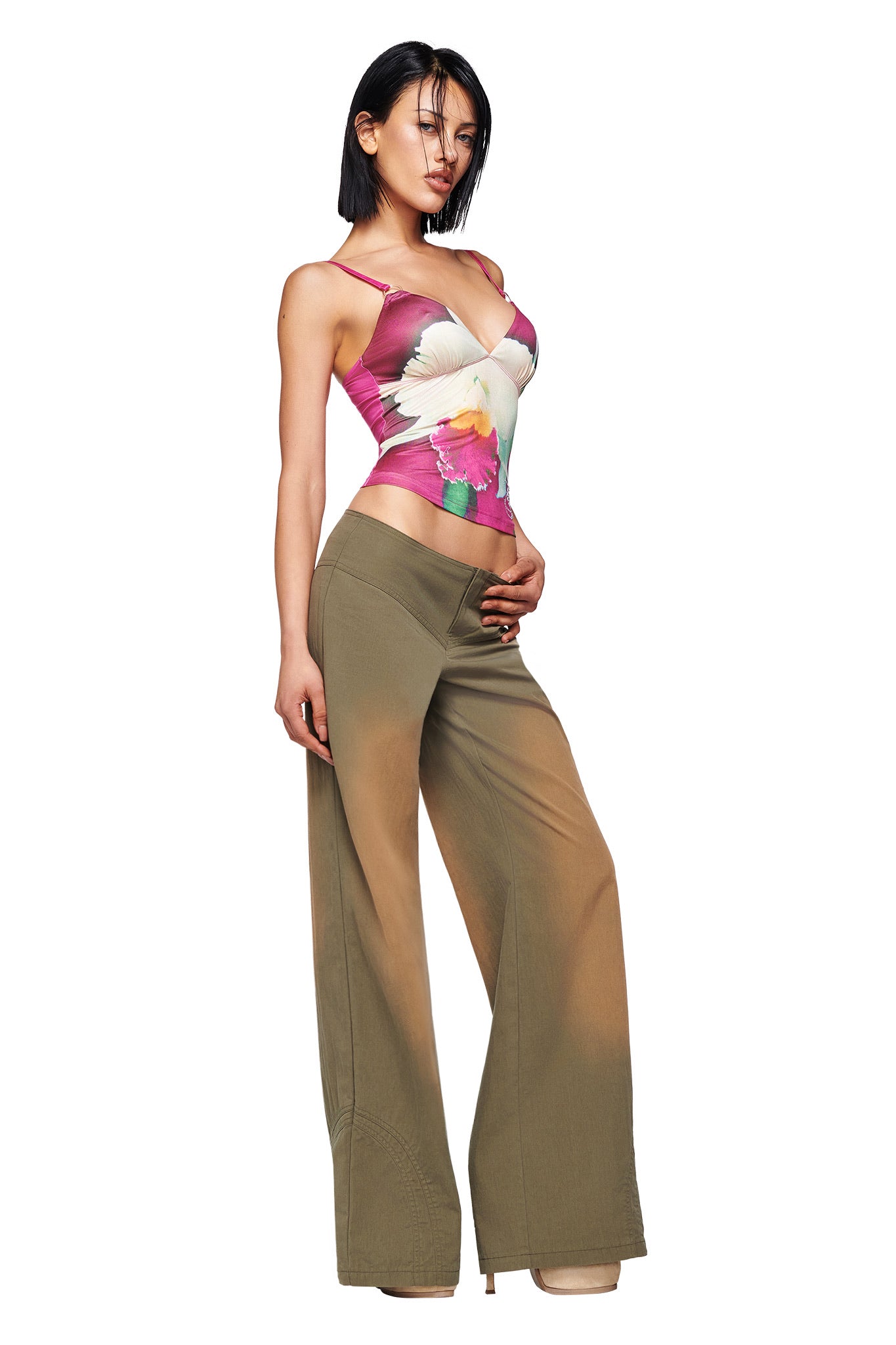 A woman poses in the ODETTA TOP - FUCHSIA by I.AM.GIA, styled with wide-legged brown pants and beige high heels, set against a white background.