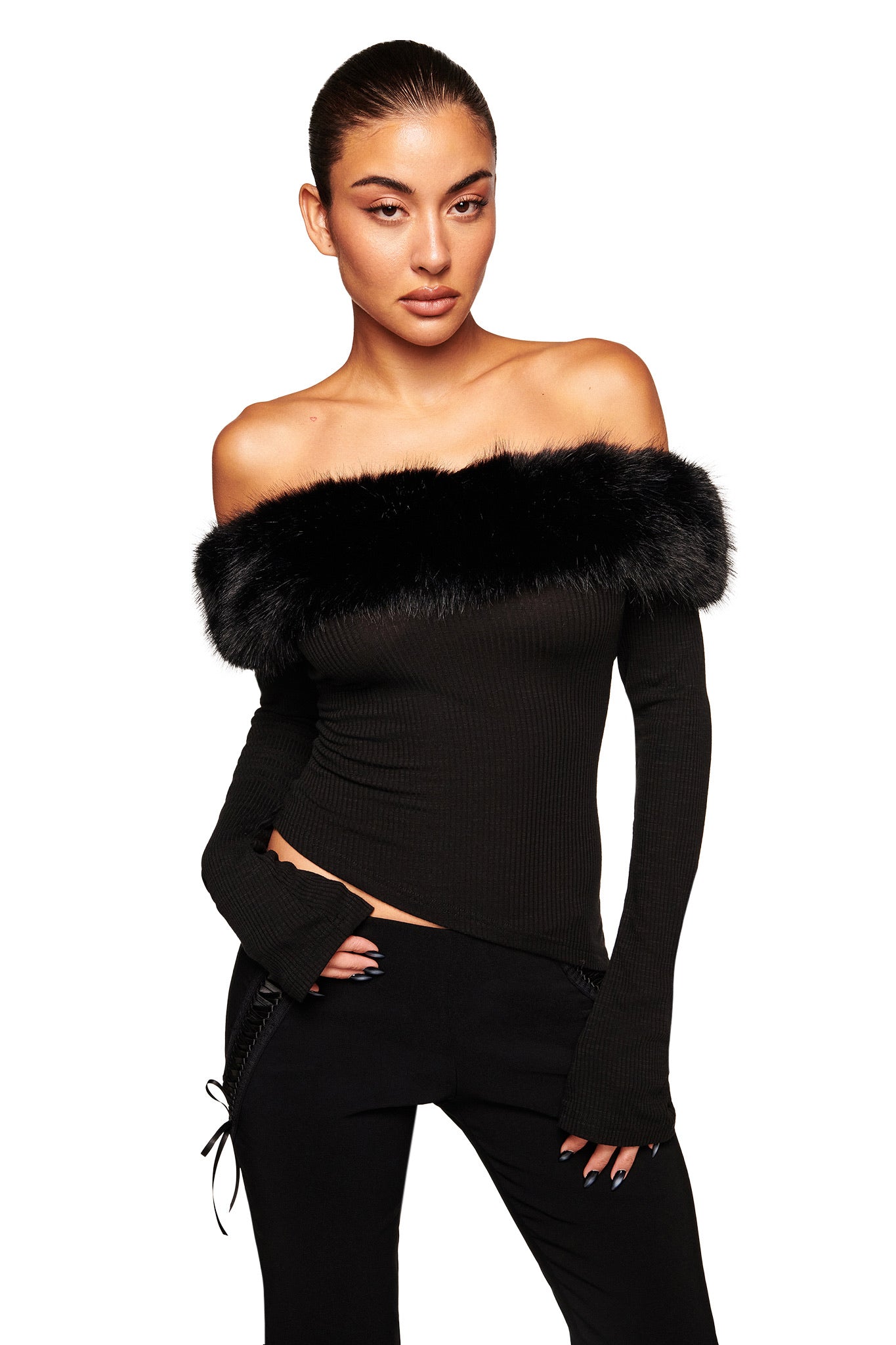 A woman exudes confidence in the I.AM.GIA CECILY TOP - BLACK, a fitted off-shoulder style with a faux fur collar and ribbed long sleeves, paired with black pants against a white background. Her hair is pulled back for a sleek look.