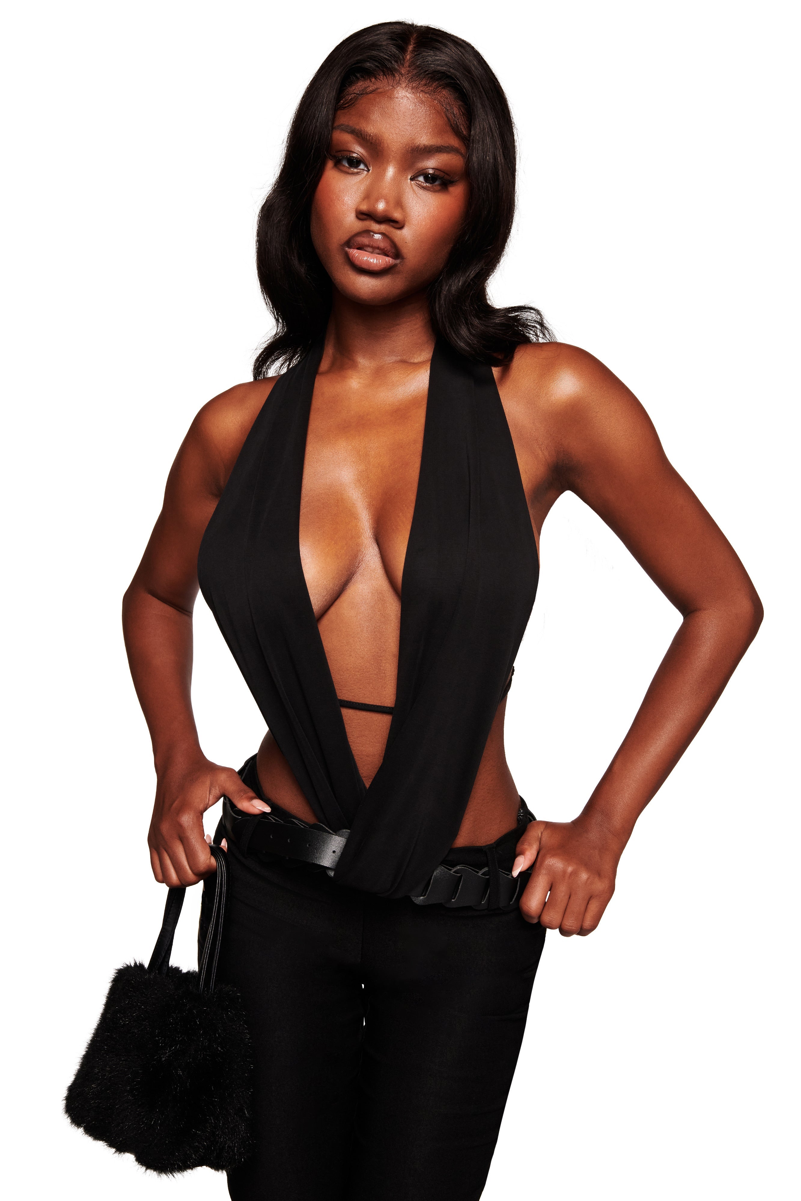 A woman exudes confidence in the I.AM.GIA SALDANA TOP - BLACK, styled with sleek black pants, a faux leather belt, and a chic small black fuzzy handbag against a plain white background.