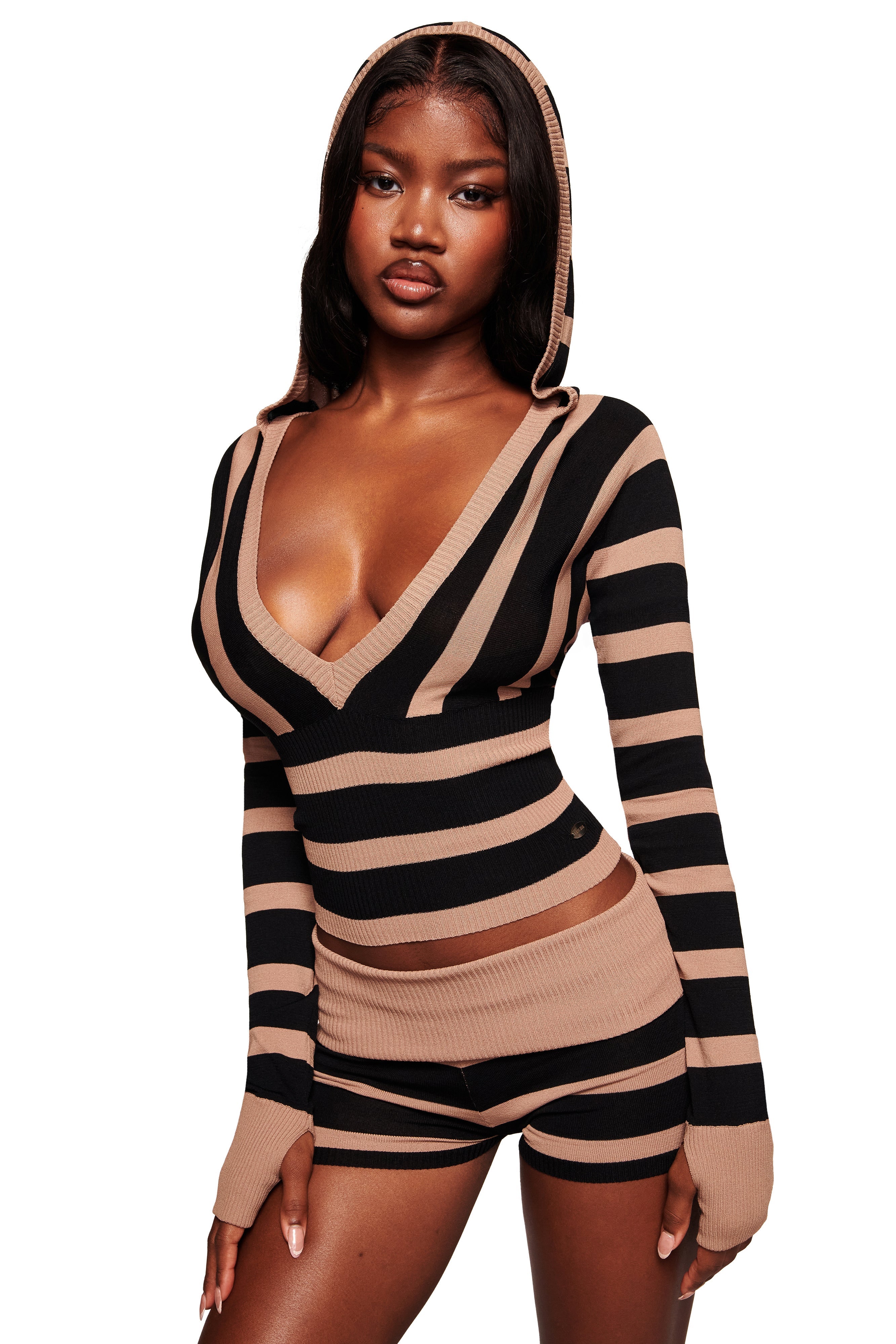 A woman poses against a white background wearing the I.AM.GIA SUZI SWEATER in black and tan stripe—a bodycon knit, long-sleeve cropped hoodie with matching shorts featuring bold horizontal stripes.