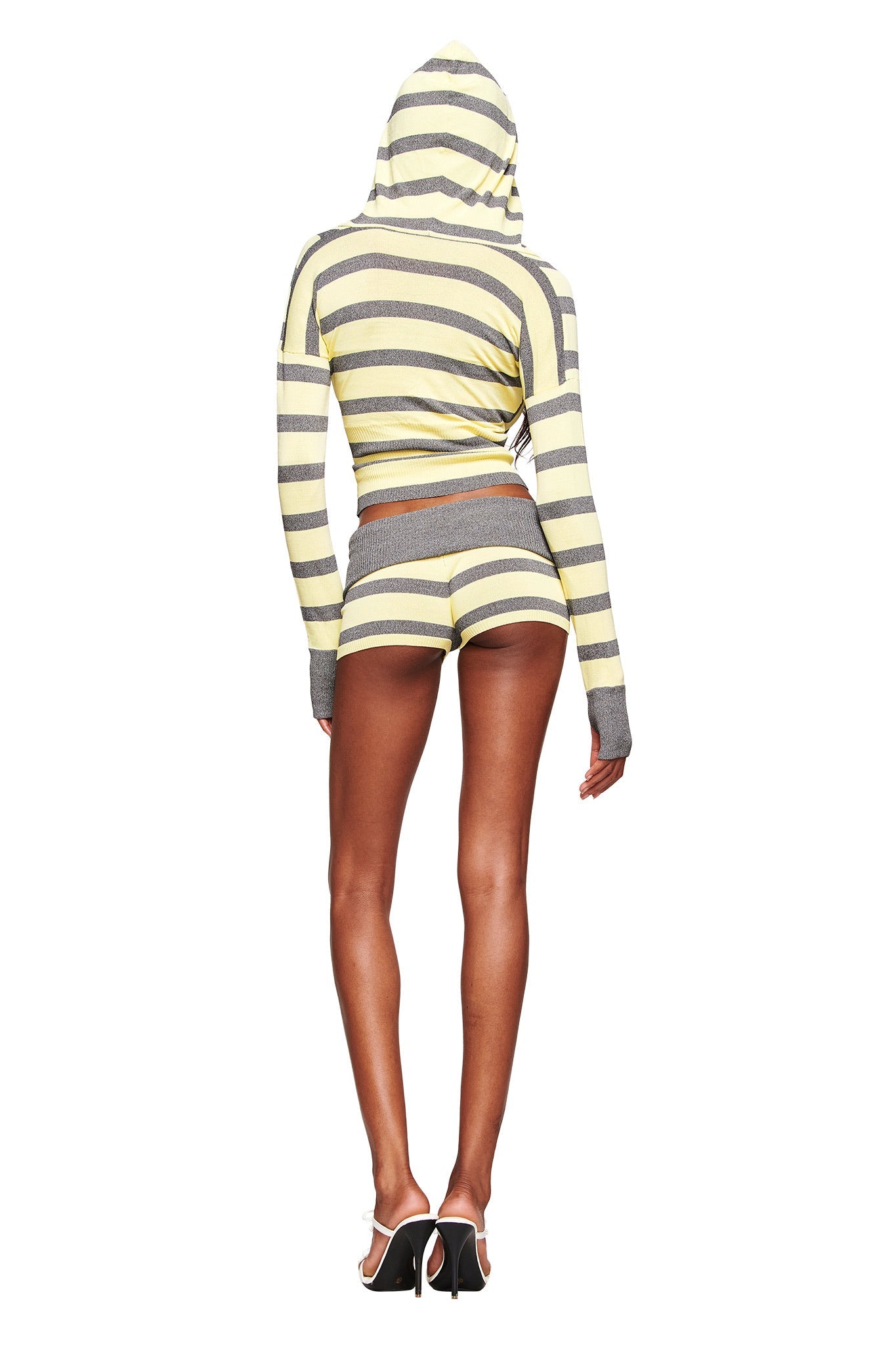 A person faces away, wearing the I.AM.GIA SUZI SHORT in yellow and grey stripes with an adjustable waistband and a matching striped crop top, paired with high heels, all against a plain white background.