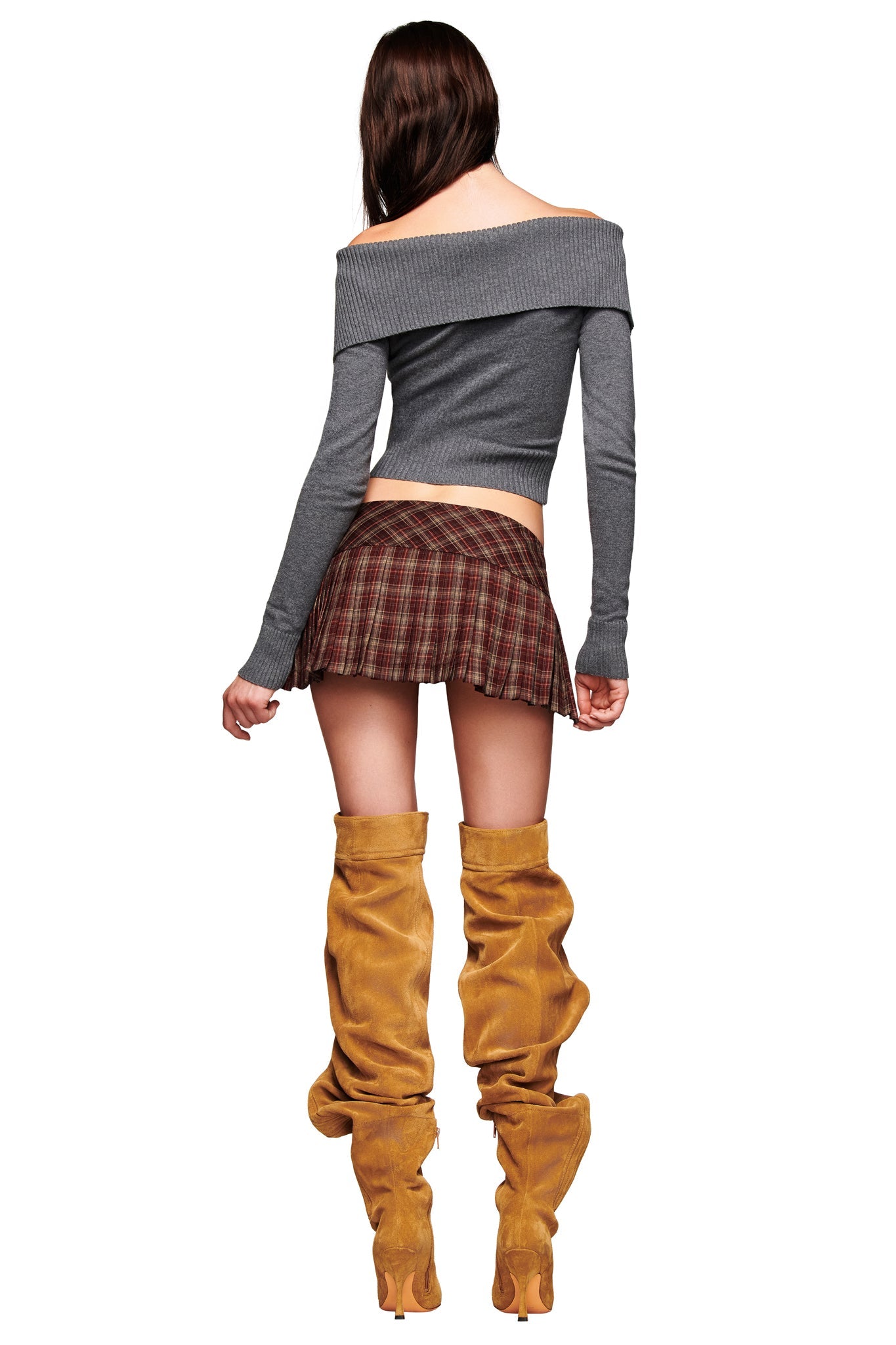 A woman stands with her back to the camera, wearing a gray off-the-shoulder sweater, tan slouchy boots, and the I.AM.GIA ROUX MINI SKORT in burgundy plaid.