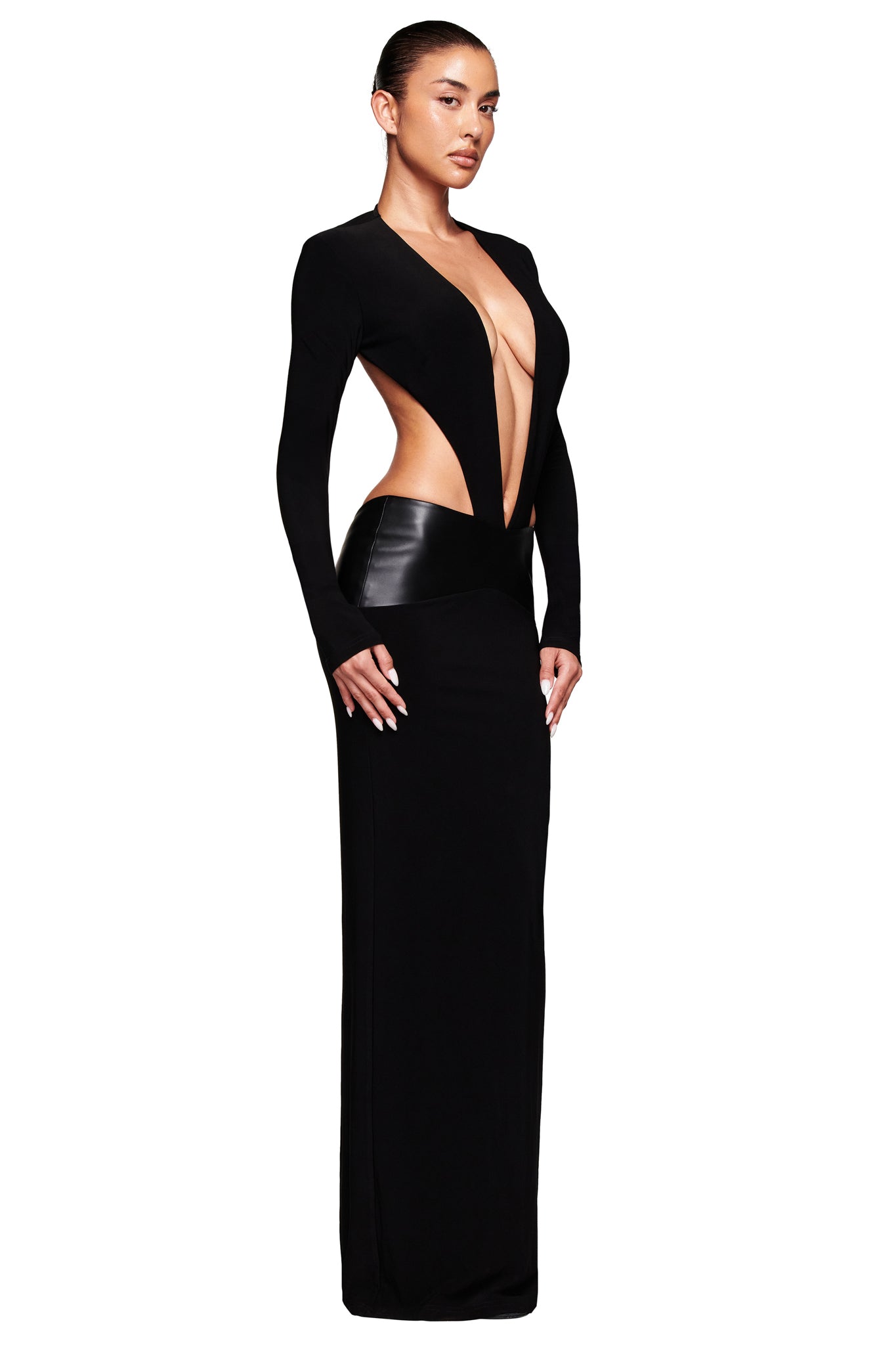 A woman poses against a white background in the I.AM.GIA CARMINA MAXI DRESS - BLACK, featuring a bold bodycon fit, deep plunging neckline, cutout sides showing midriff and lower back, and a faux leather waistband. Hair pulled back for a sleek look.