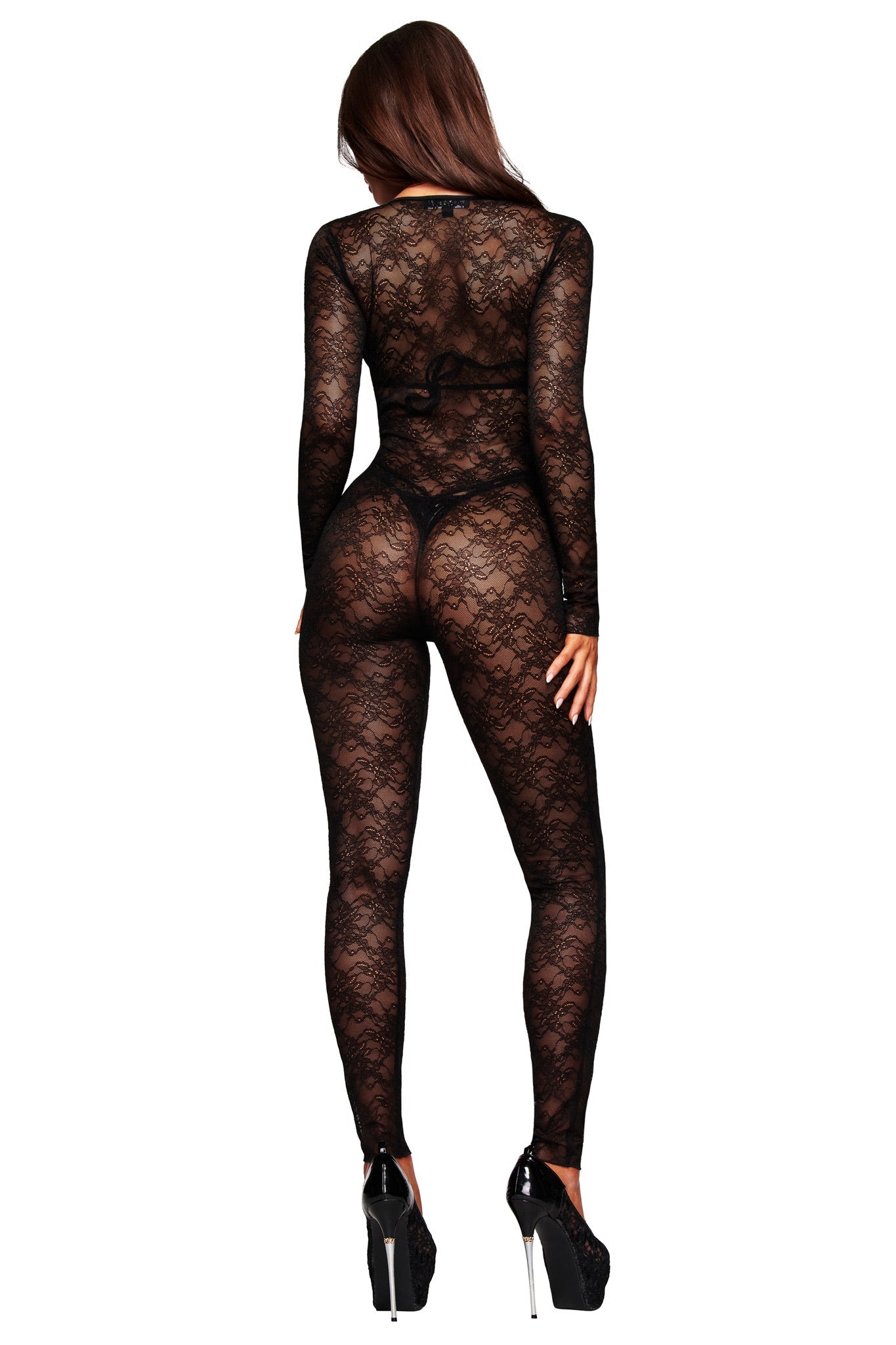 A woman with long brown hair and black heels models the I.AM.GIA TIGRA CATSUIT - BLACK, a sheer lace design with long sleeves and full-length legs, shown from behind against a plain white background.