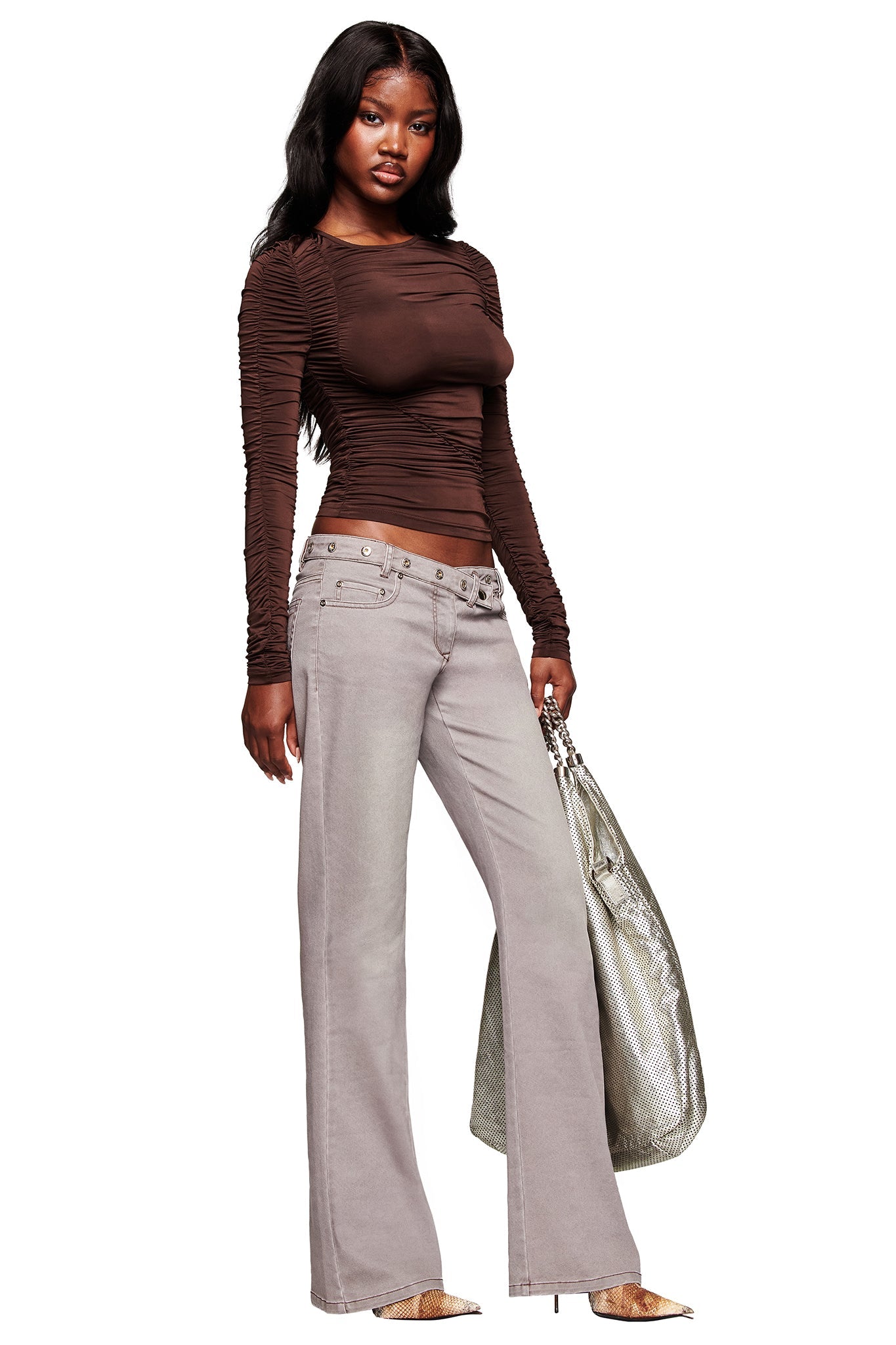 A woman stands holding a large silver bag, wearing a sheer brown ruched top, I.AM.GIA GREER PANT - GREY with wide legs and grommet details, plus snake-print pointed-toe shoes.