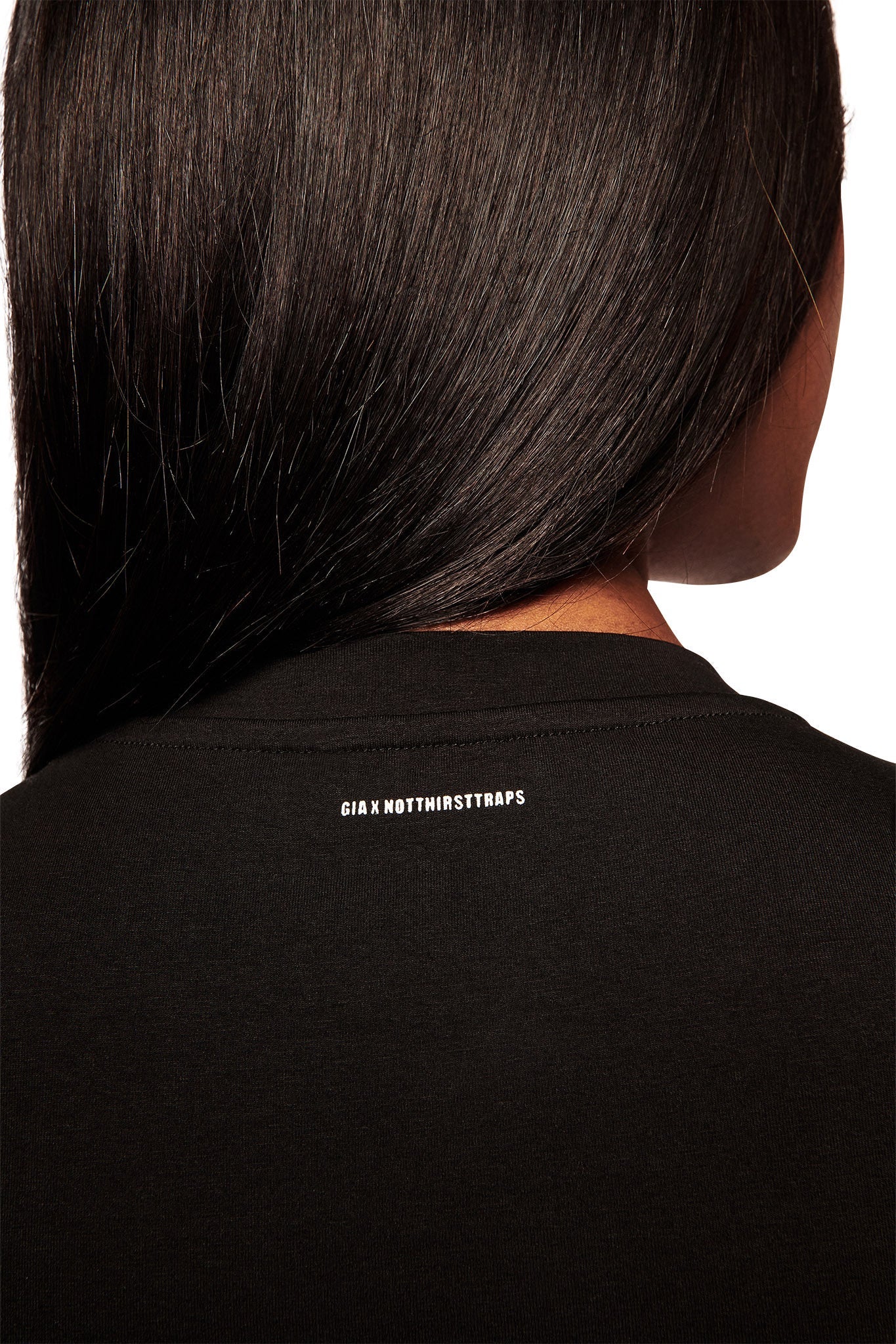 The back of a person with straight, dark hair wears the I.AM.GIA POLINA TEE - RESEARCH, a black graphic t-shirt with small white text "CIA X NOTHINGSTRAPS" near the neckline. The background is white.
