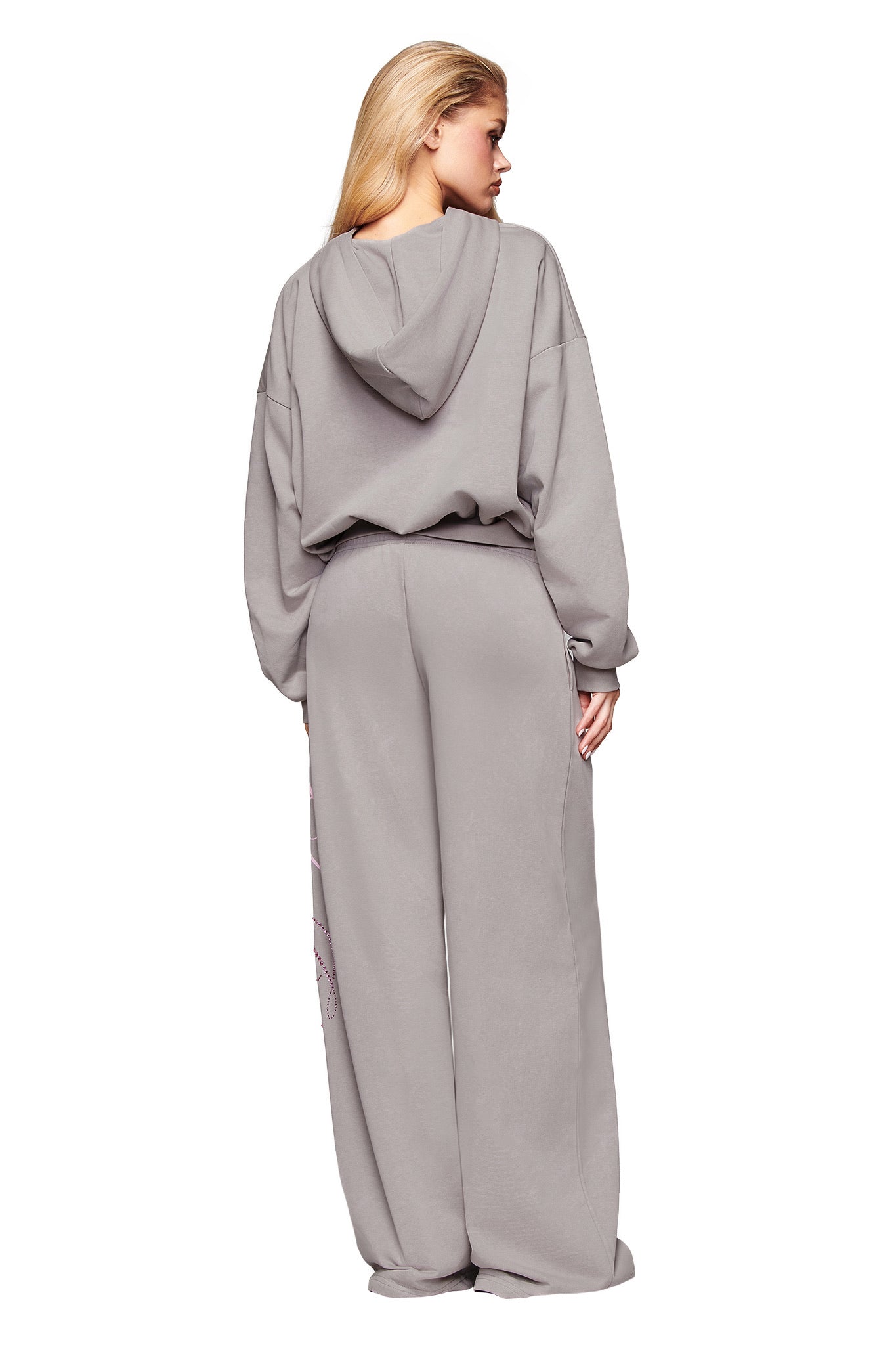 A person with long blonde hair is standing and facing away, wearing the I.AM.GIA KADE HOODIE in grey and matching wide-leg sweatpants.