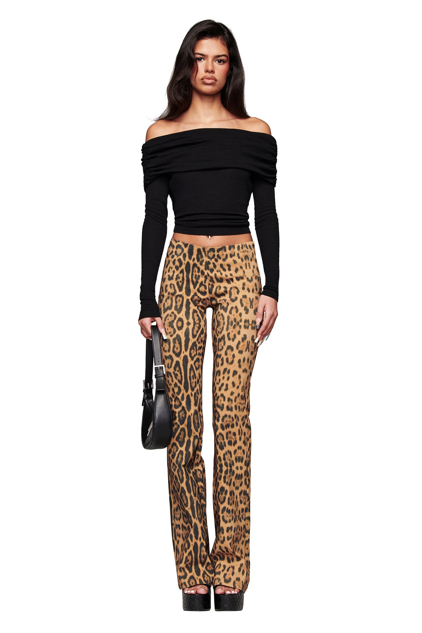 A woman faces forward wearing the I.AM.GIA VEYRA LONG SLEEVE TOP in black, paired with high-waisted leopard print pants, black platform shoes, and holding a black handbag against a white background.