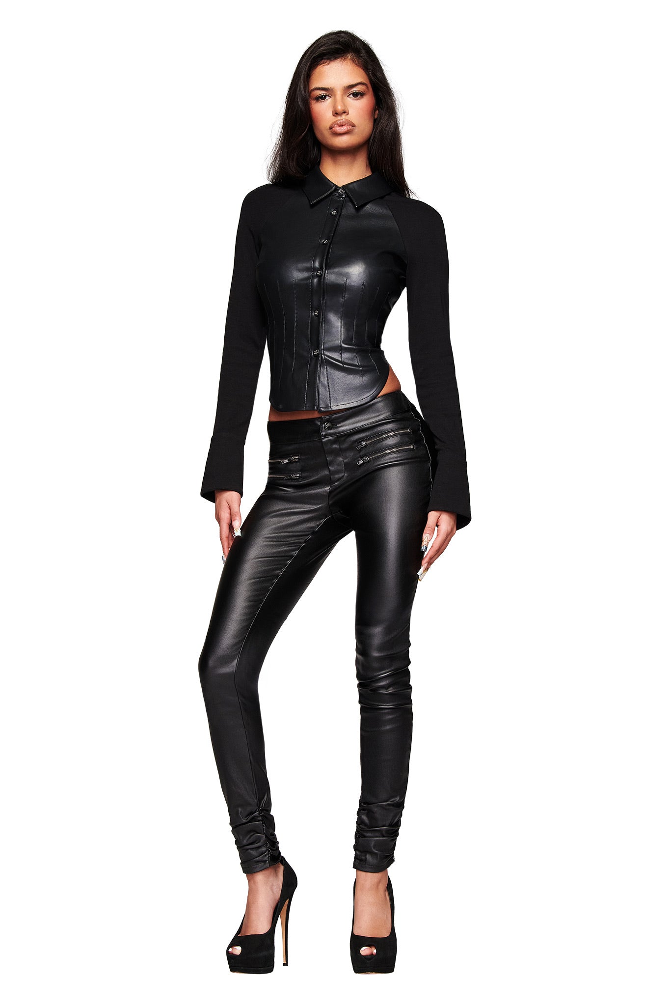 A woman with long dark hair and a confident expression models the I.AM.GIA JETT PANT in black against a white background, pairing the skinny jeans with a fitted black leather jacket and high-heeled shoes.